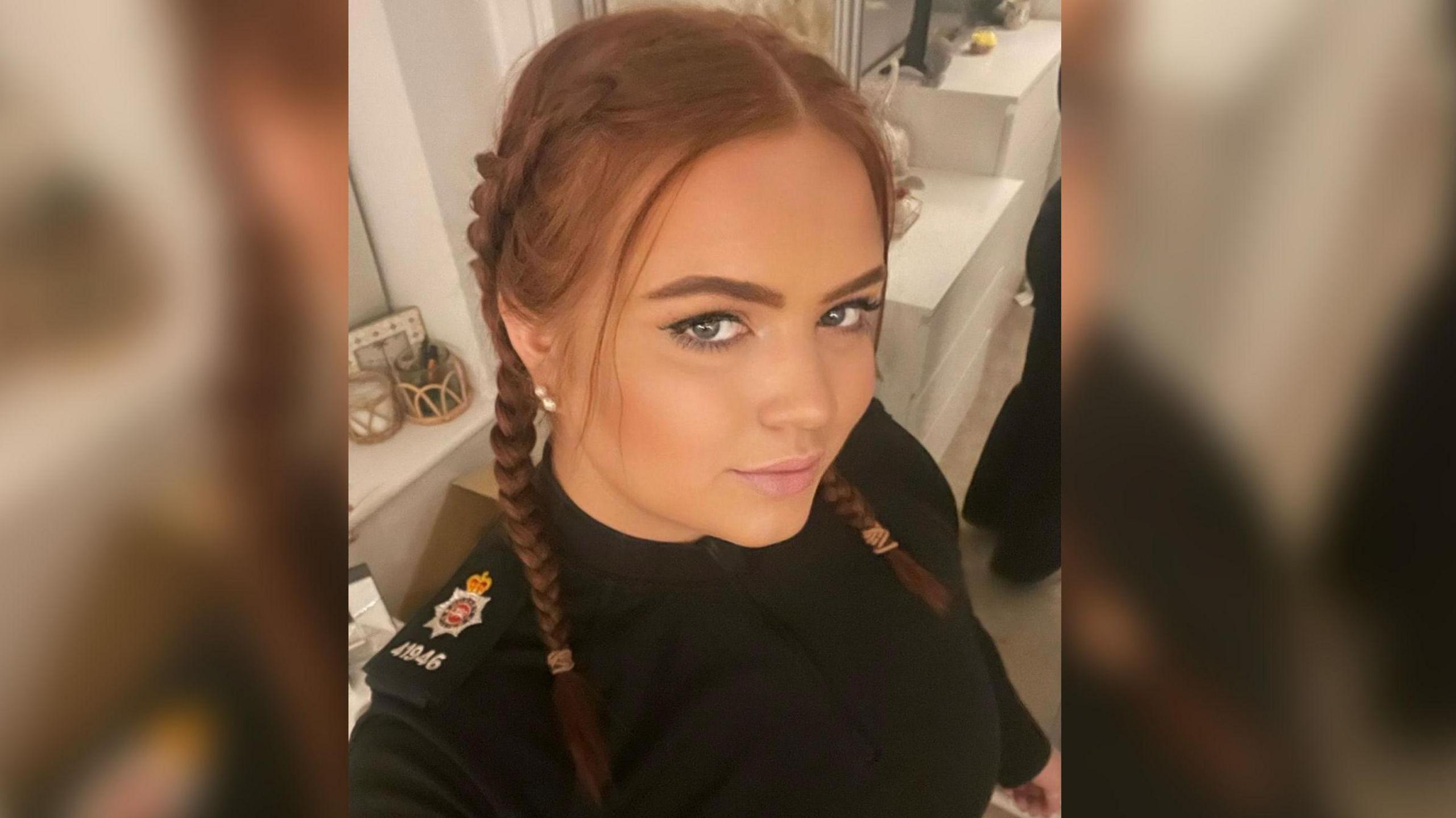Hannah in a selfie looking up at the camera. She has her hair in two plaits and is wearing her police top with a badge on her shoulder.