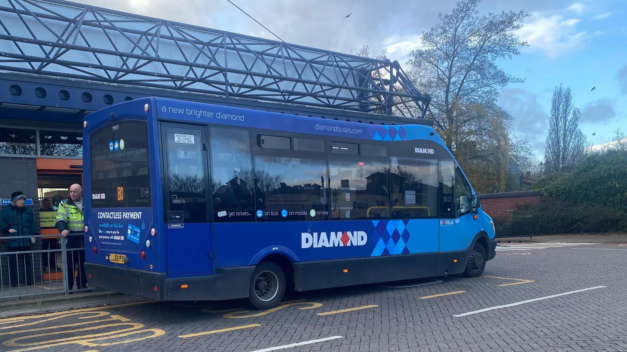 A blue bus number 80 bus with the word Diamond is parked in front of a bus station with a blue metal structure for a roof. It is a single decker, small bus.