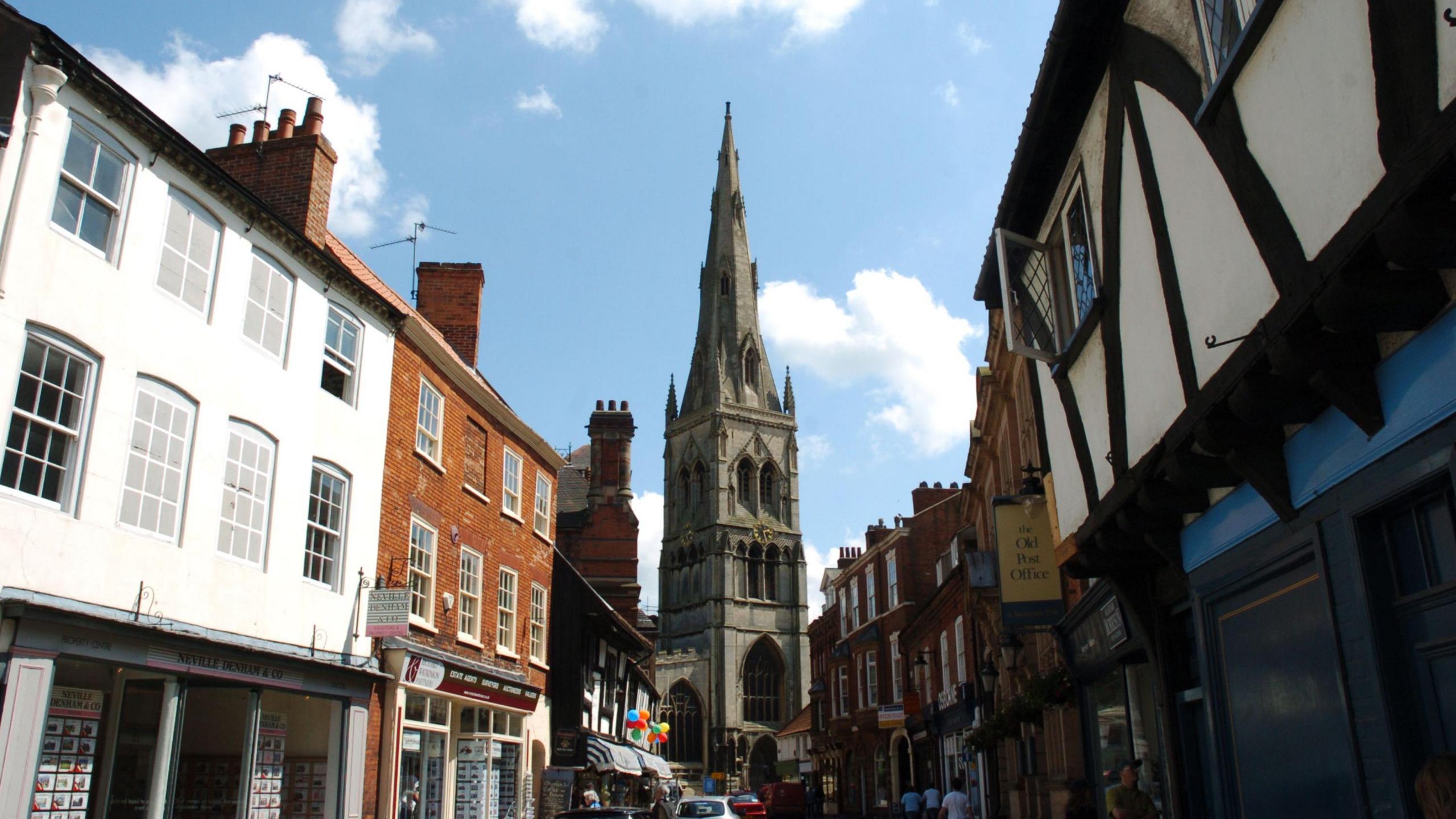 A classic church tower with a high spire looms over a historic town street