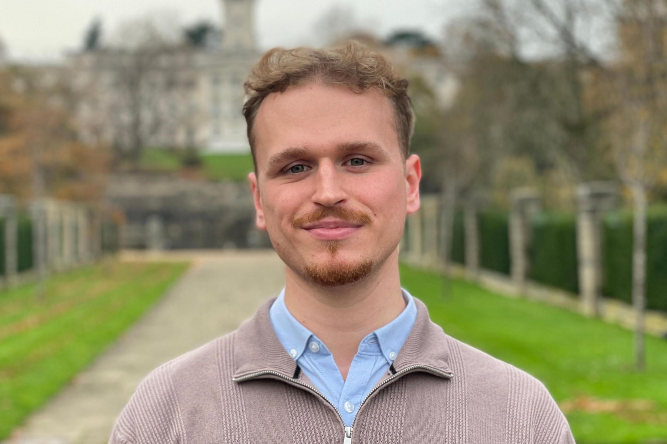 Max Hegarty standing in front of the gates to Highfield Park with the university's Trent Building in the background