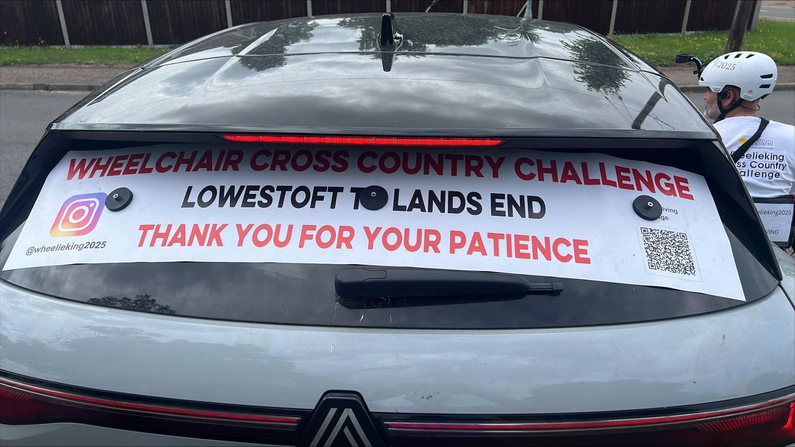 A photo of the rear of the support car. A poster over the window reads: "Wheelchair cross country challenge. Lowestoft to Land's End. Thank you for your patience."