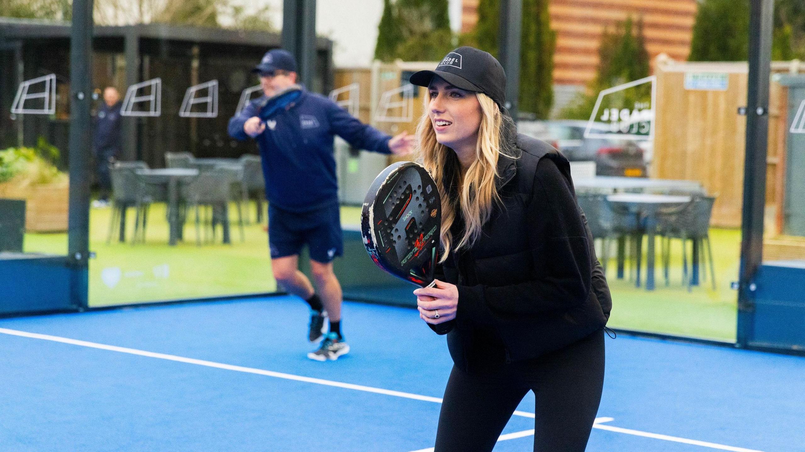 A woman waits at the net on a padel ball court with her racquet raised