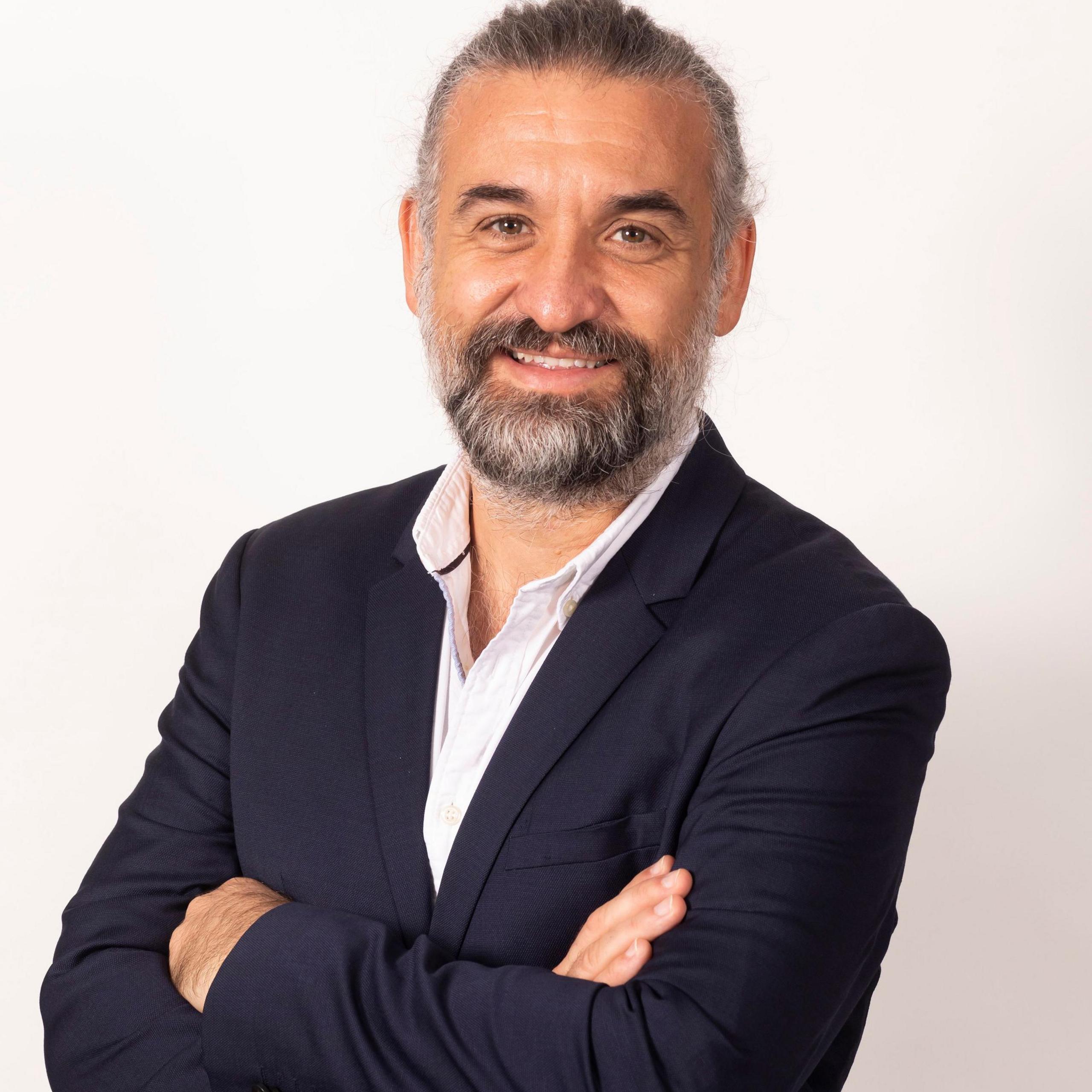 Juanra Gonzalo, in a suit, smiling with his arms folded