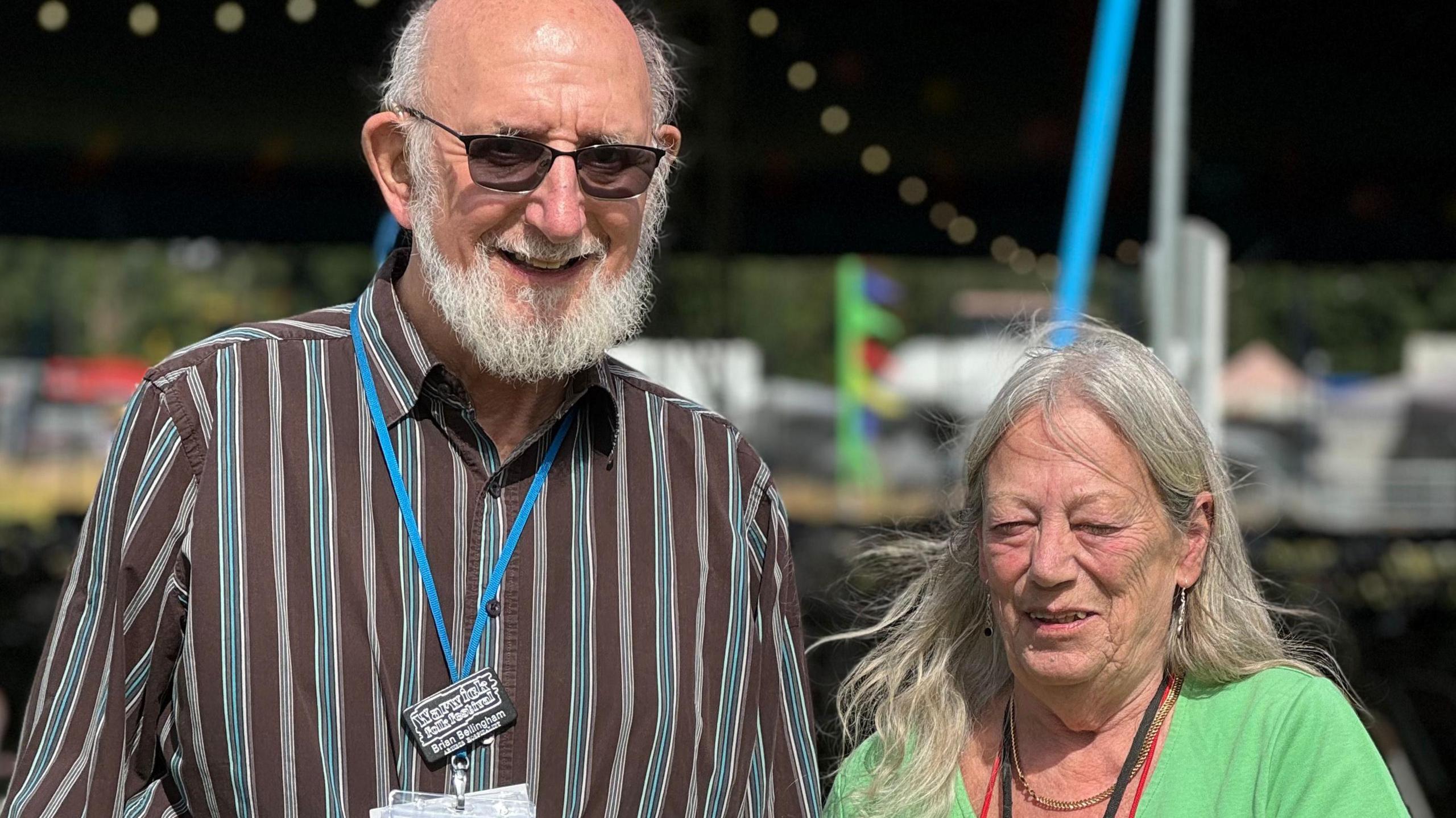 Bryan is wearing a black and blue striped shirt and a blue lanyard. Rita Bellingham has a green top