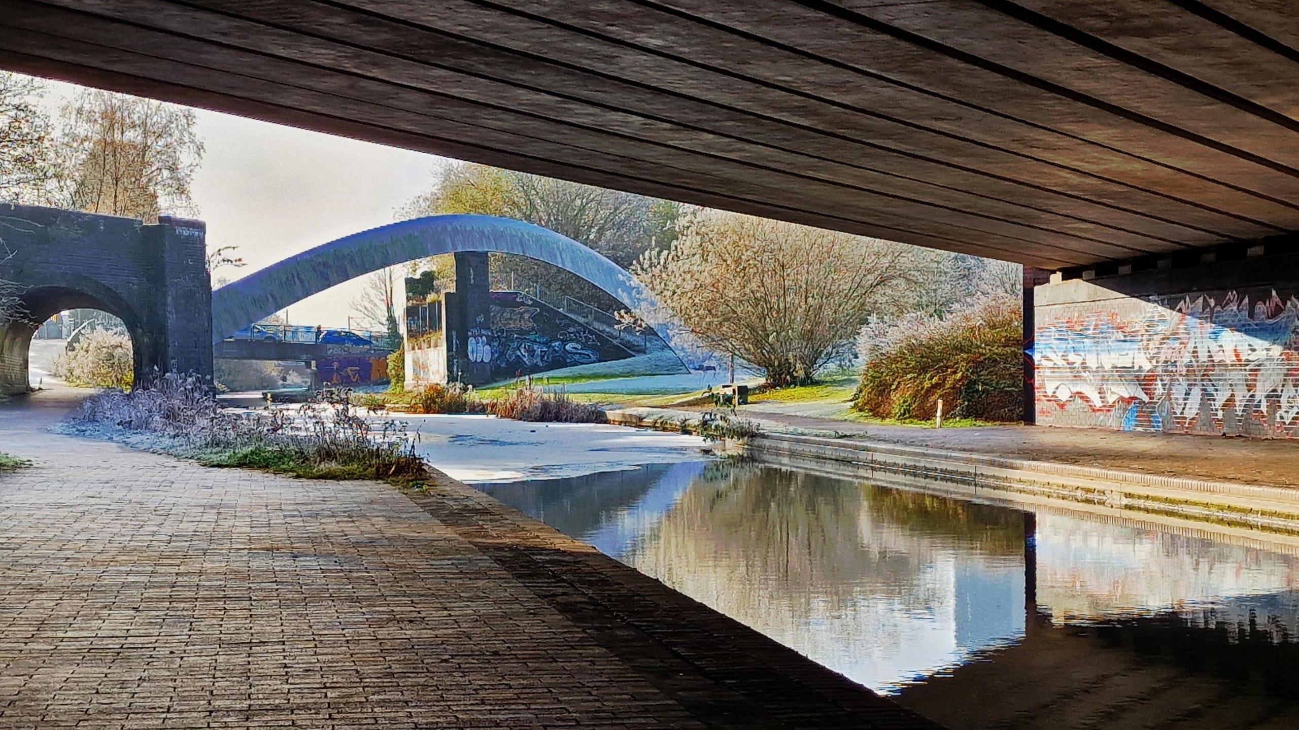 A bridge stands over the canal with graffiti painted on the walls. More bridges and arches can be seen in the distance 