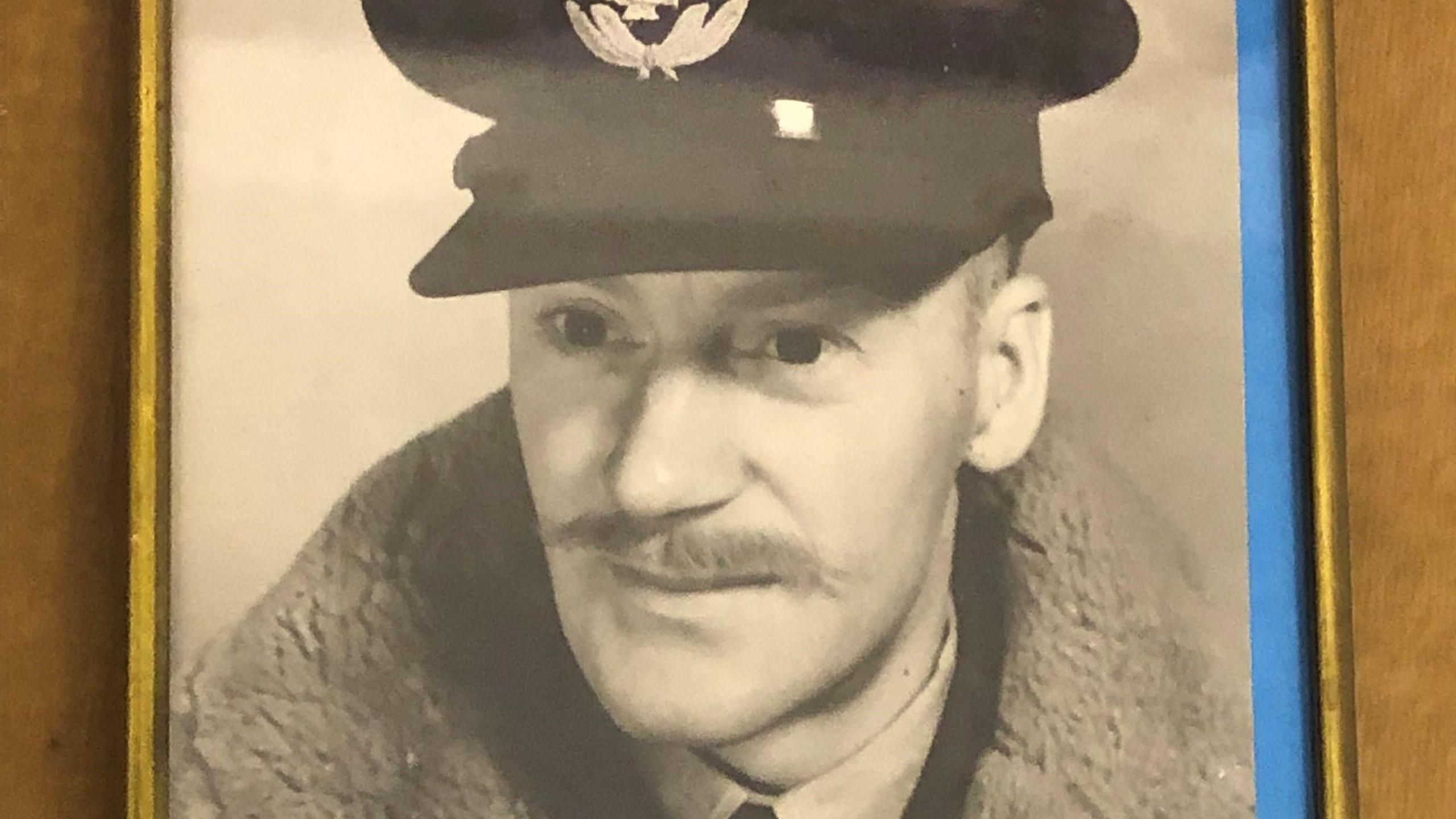 A World War 2 era photograph of Flying Officer Norman McEwan, in RAF uniform and flying jacket. He has a slim handlebar moustache.