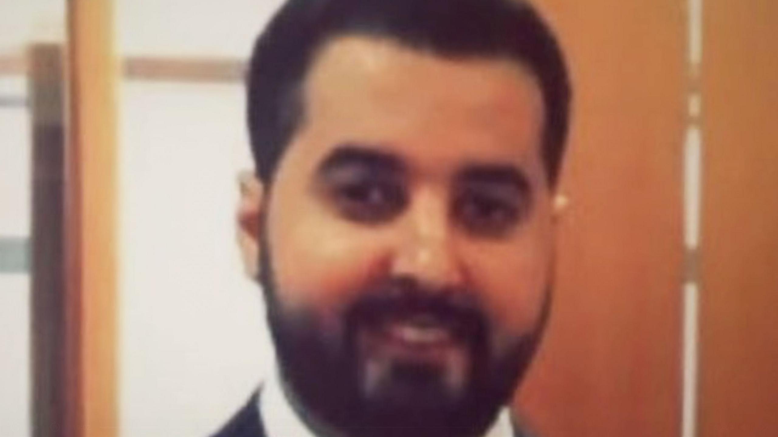 Bader Alomair smiles at the camera - he has dark hair and a dark beard, and appears to be wearing a white shirt and dark suit