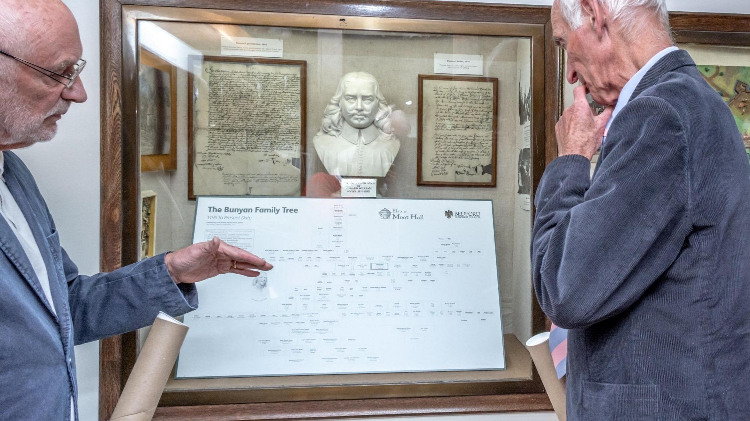 Two smartly dressed men read and consider the family tree printed on a piece of paper in front of them