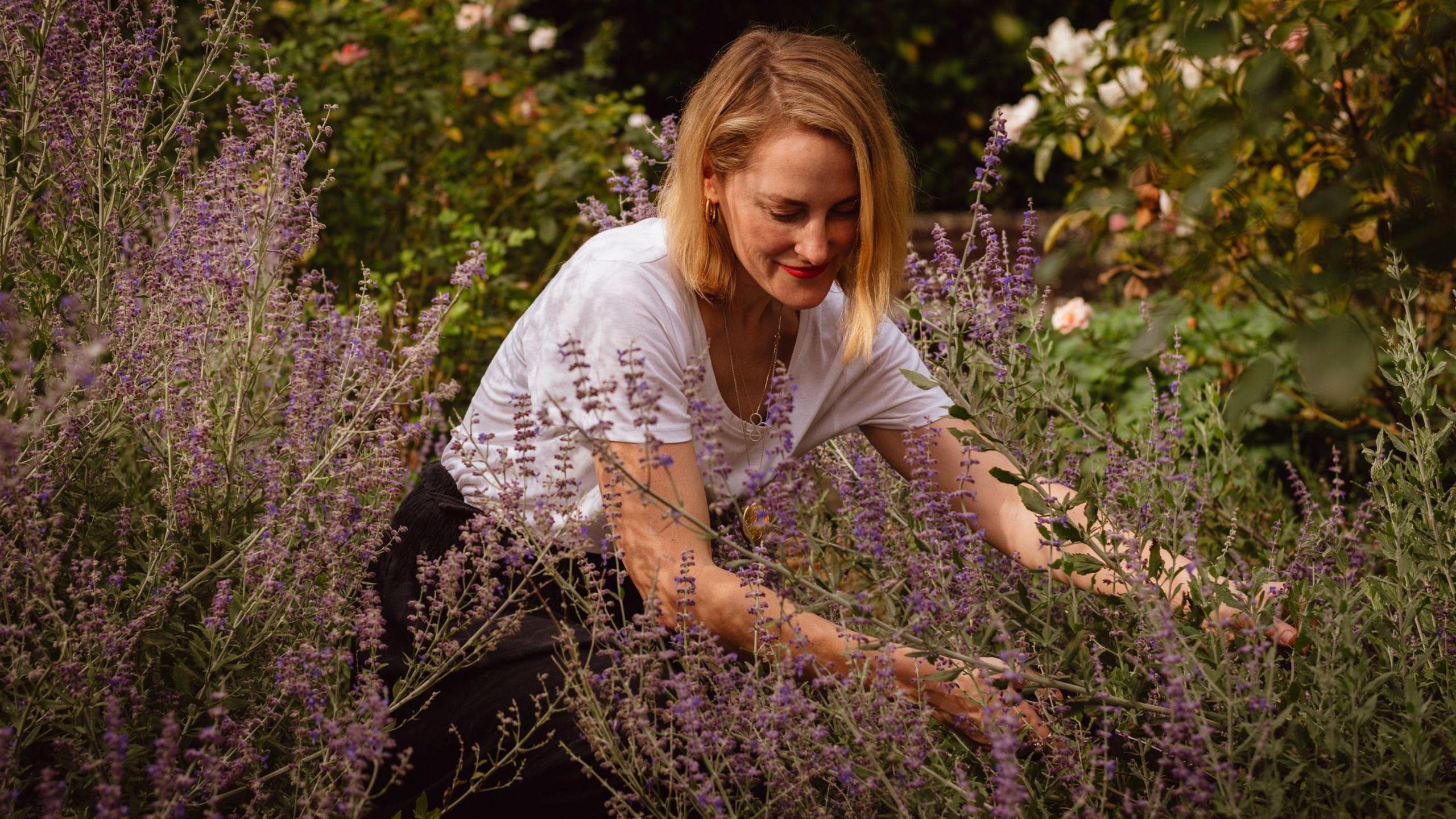 Louise Avery in a white t-shirt foraging for a purple coloured plant