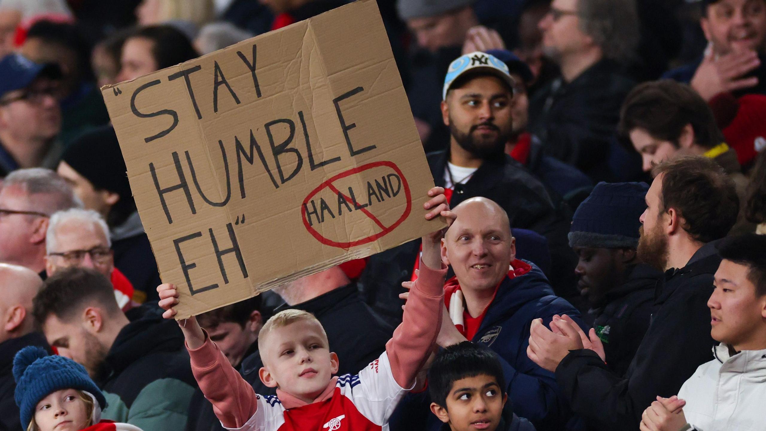 An Arsenal fan holds up a banner saying 'stay humble', aimed at Erling Haaland