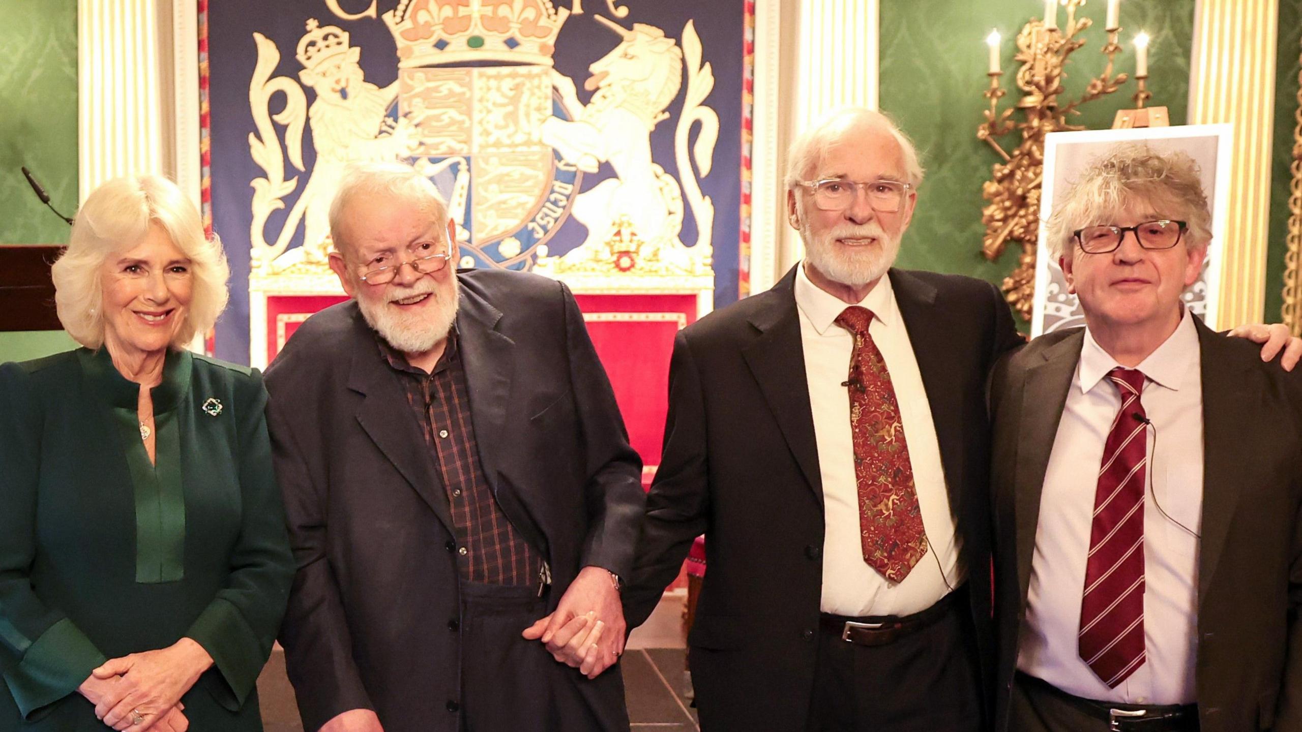 The Queen poses with, poet Michael Longley, actor Ian McElhinney and poet Paul Muldoon, as she attends Northern Ireland: Poets and Their Place. The Queen wears a dark green dress while the poets all wear suits. Longley has no tie, the others have red ties.