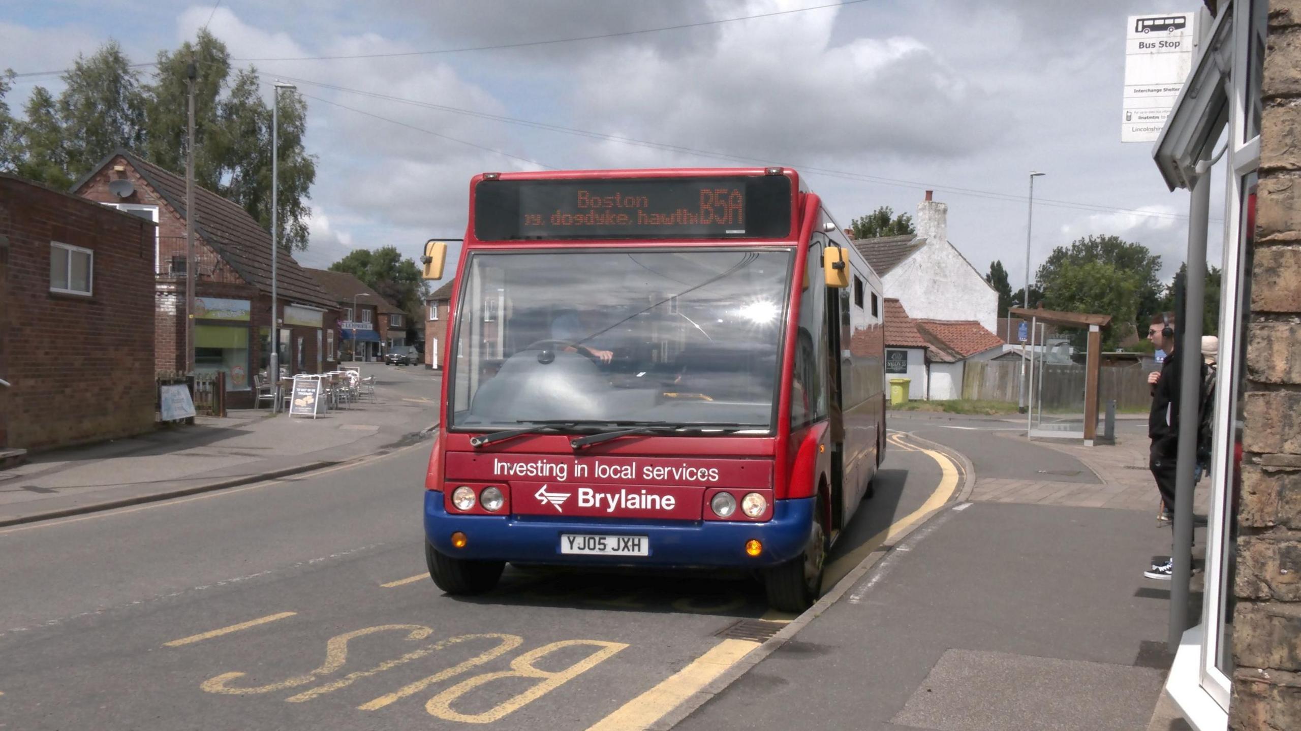 A small red bus, with Boston set as the destination on the front, pulled up at a bus stop