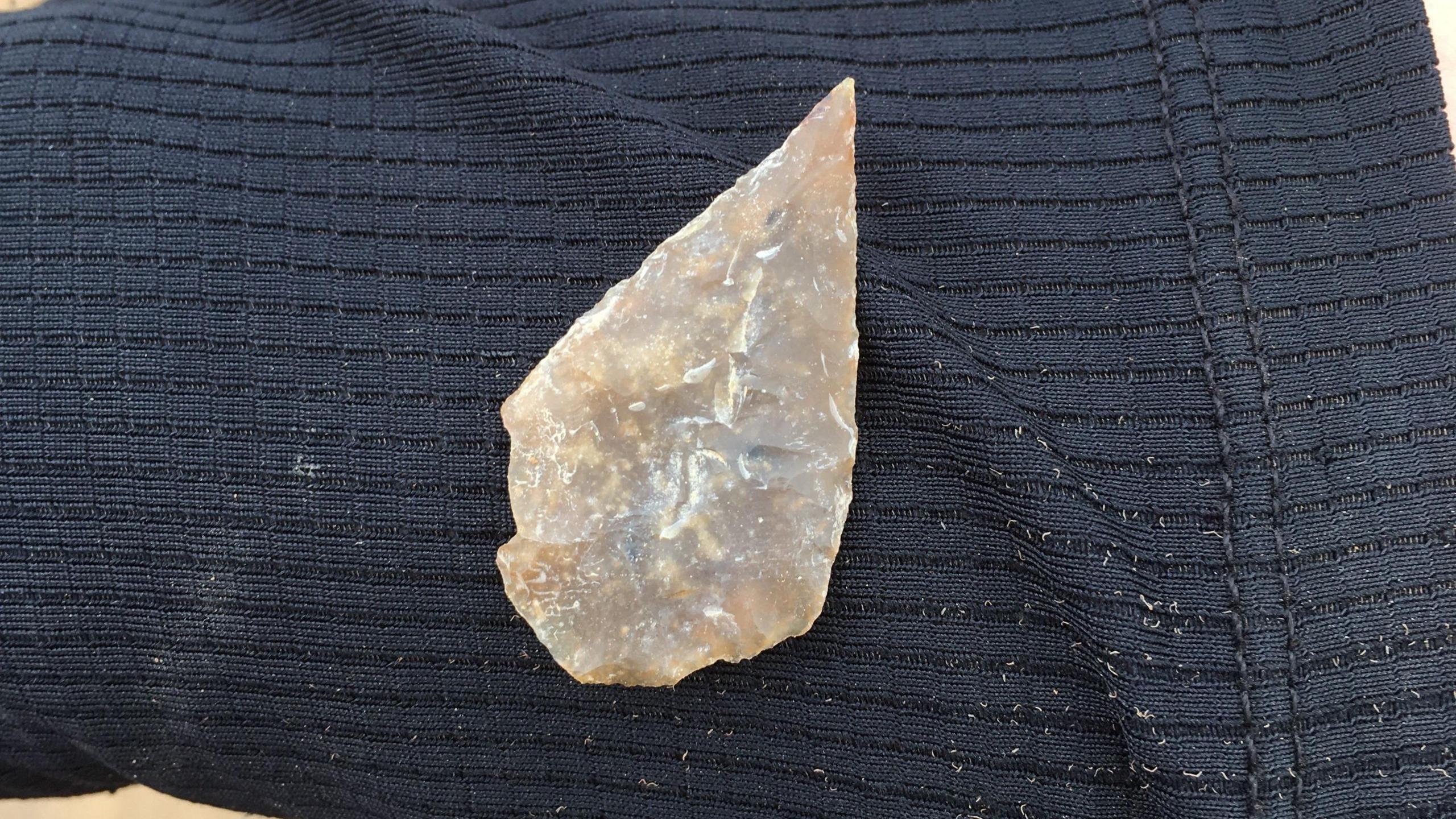 An archaeologist holds up an arrowhead on their black sleeve.