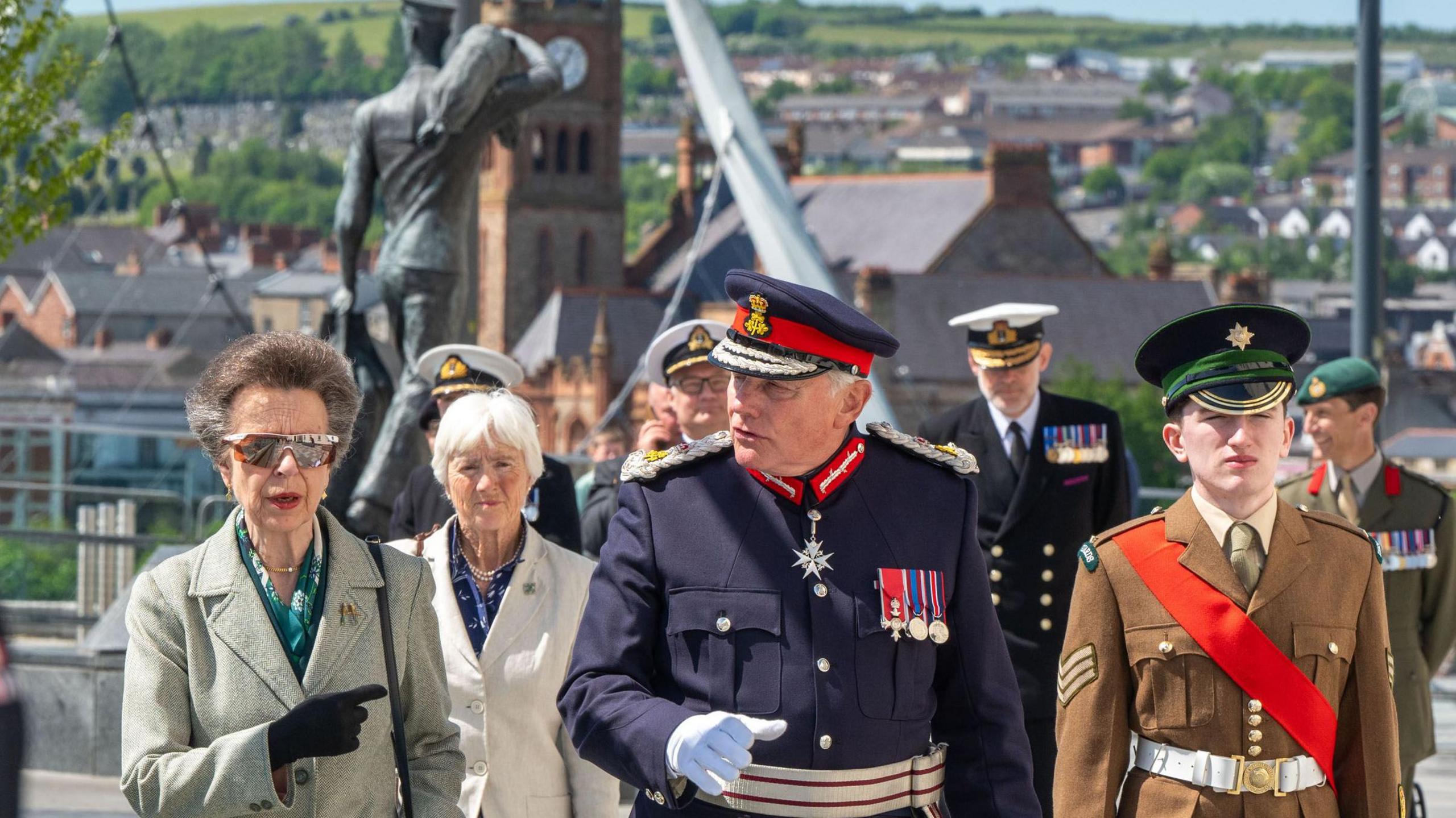 A groups of people, some in naval uniform, walk across Derry's Ebrington Square. Two of the people are women, in the company of five uniformed men