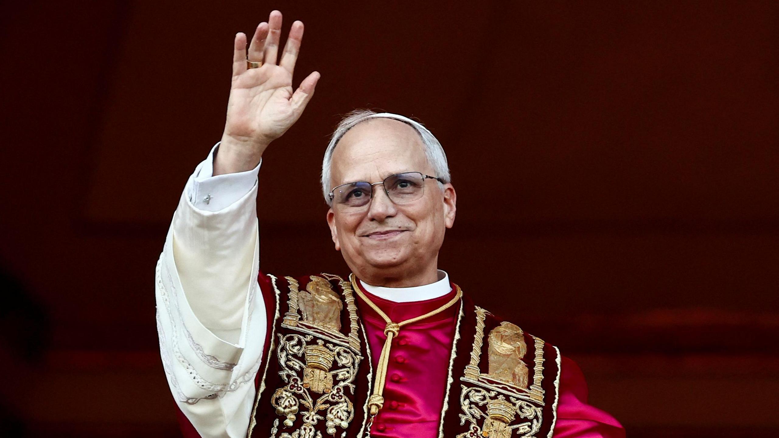 Pope Leo XIV standing on the balcony of St Peter's Basilica at the Vatican. He is waving and smiling.