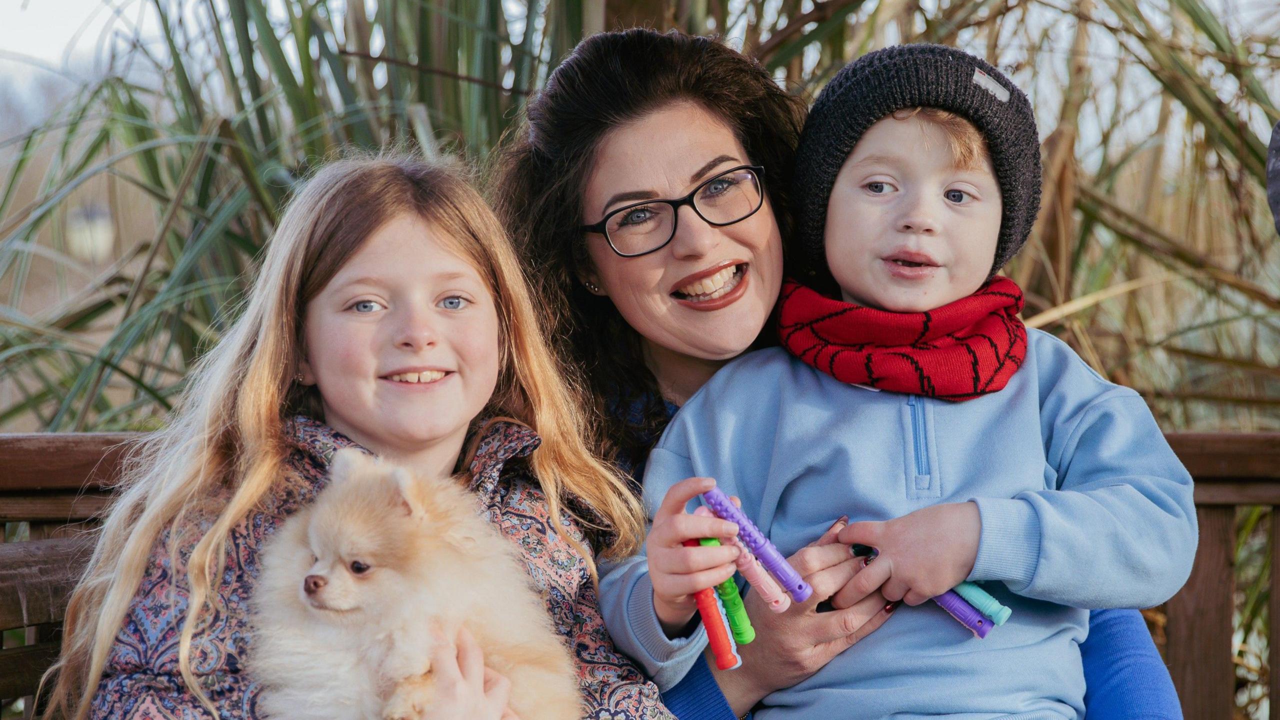 A family, including Rozalyn, mum Abbie and Rory, are sat outside smiling. Rosa the Pomeranian is being held by Rozalyn on the left hand side. 
