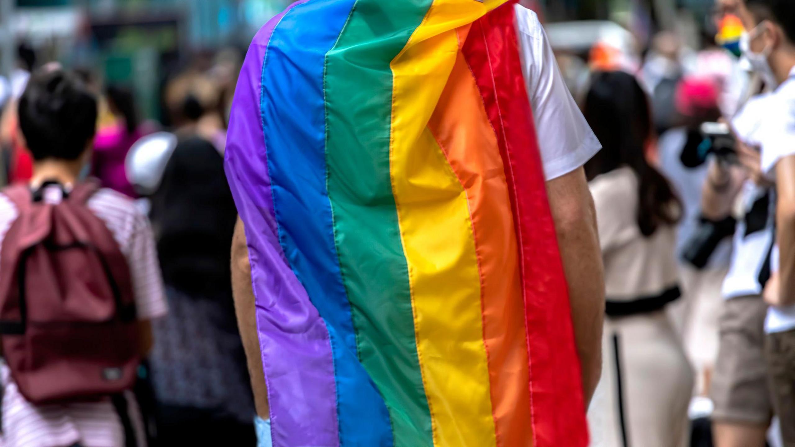 A person draped in a rainbow flag like a cape. 