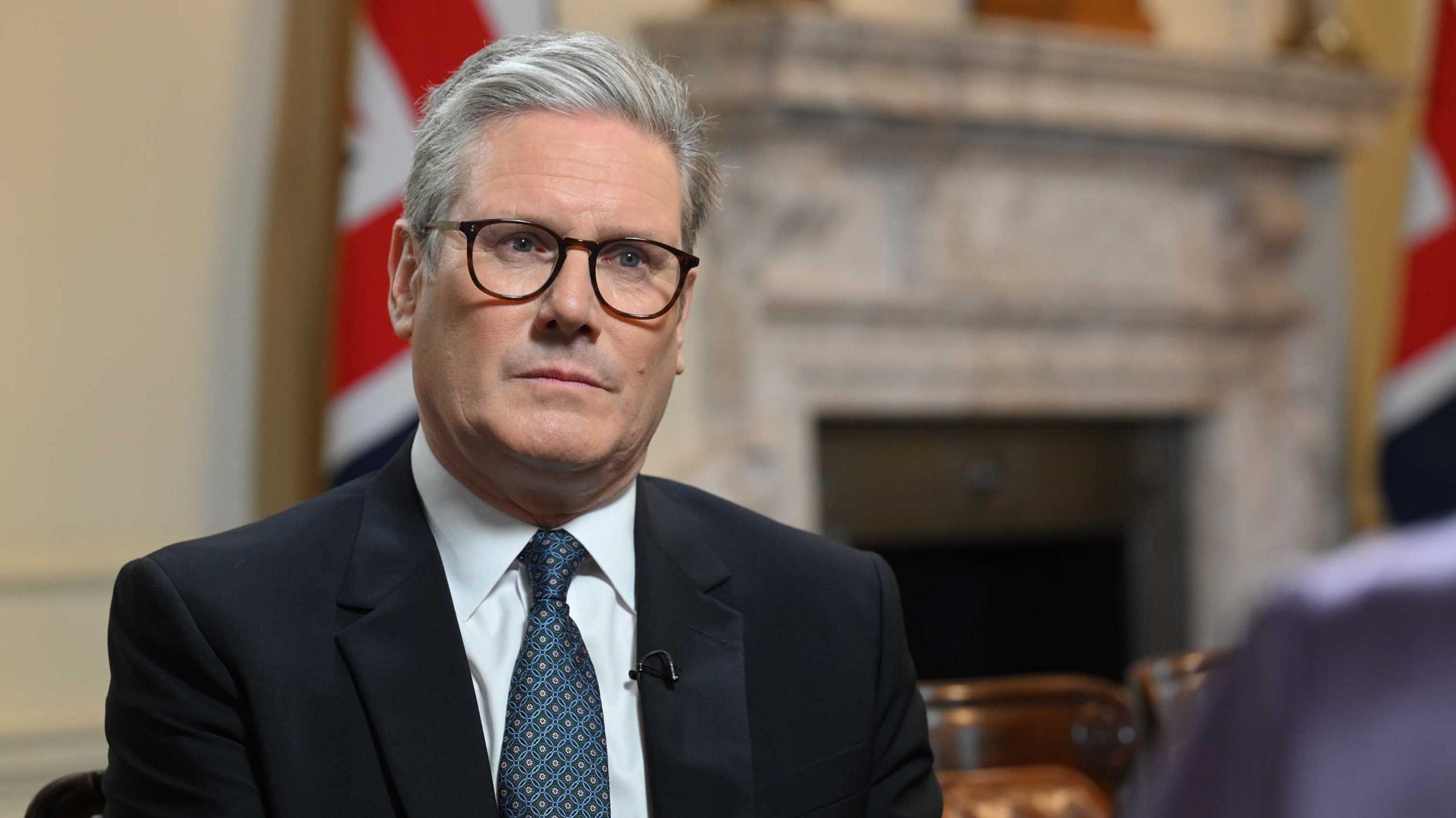 Prime Minister Keir Starmer, wearing glasses and a dark suit, sits down as he faces Laura Kuennsberg in Downing Street