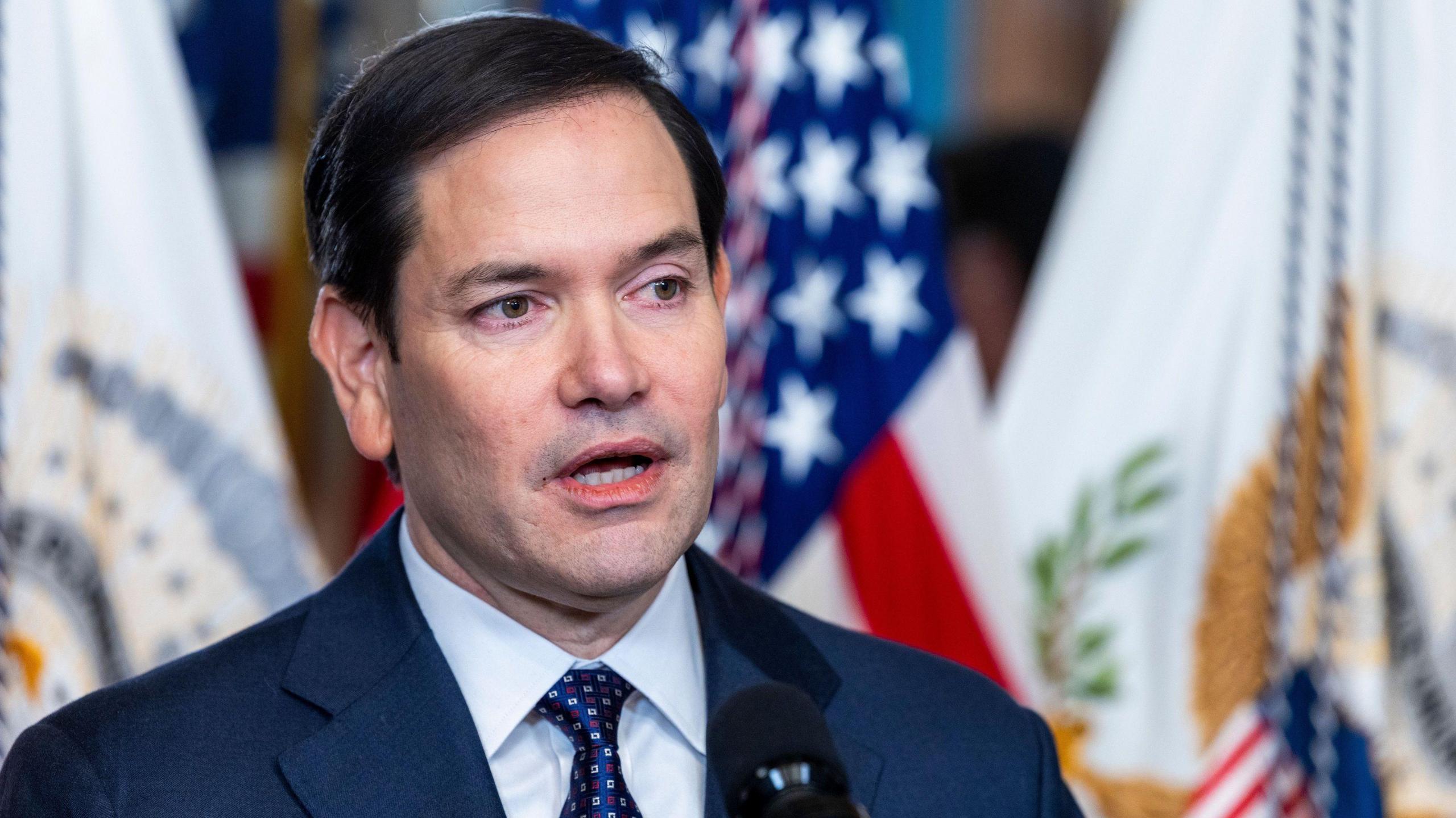 Marco Rubio stands in front of flags 