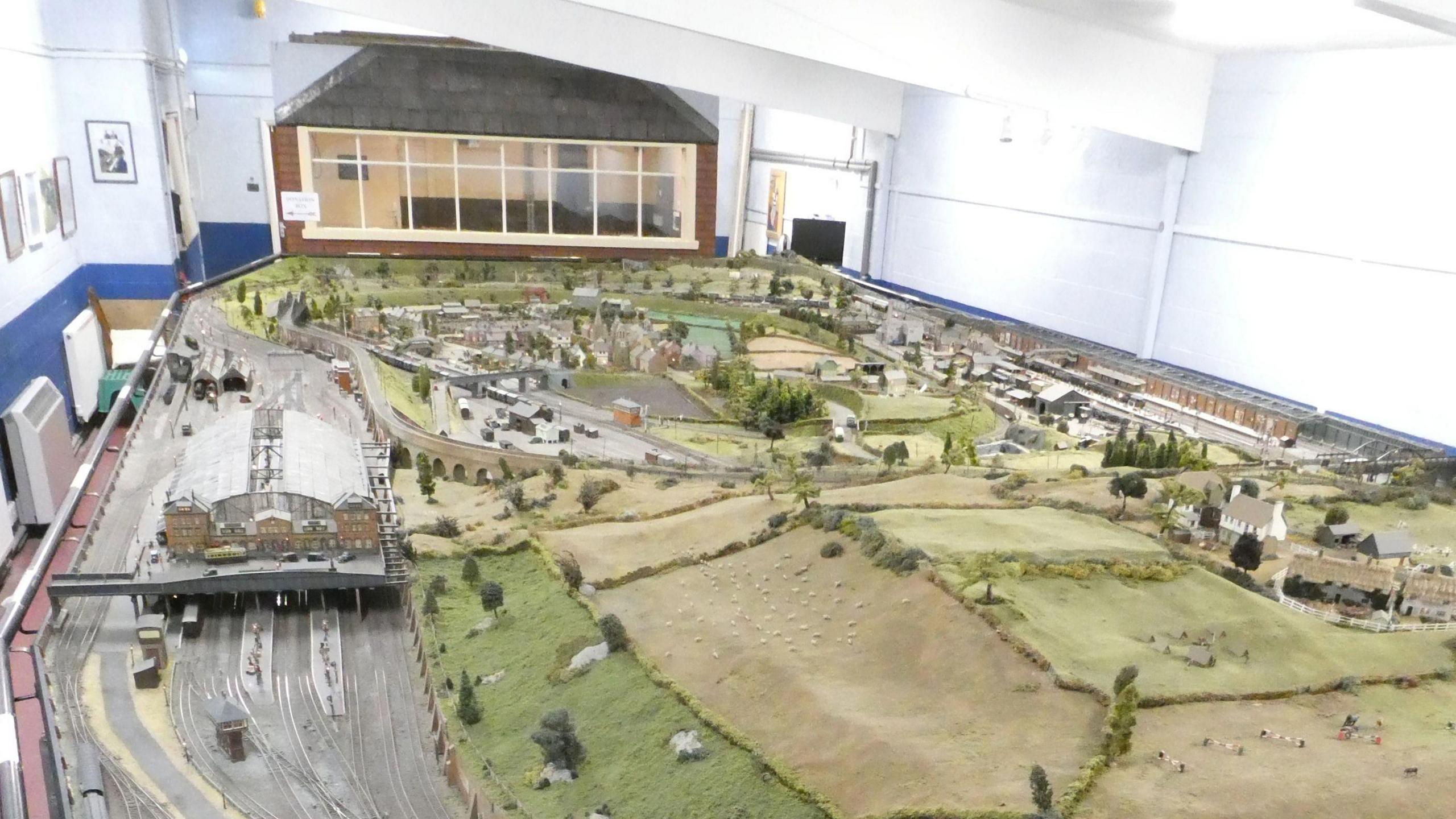 The model railway has tracks, green fields and houses. A signal box sits at the end.