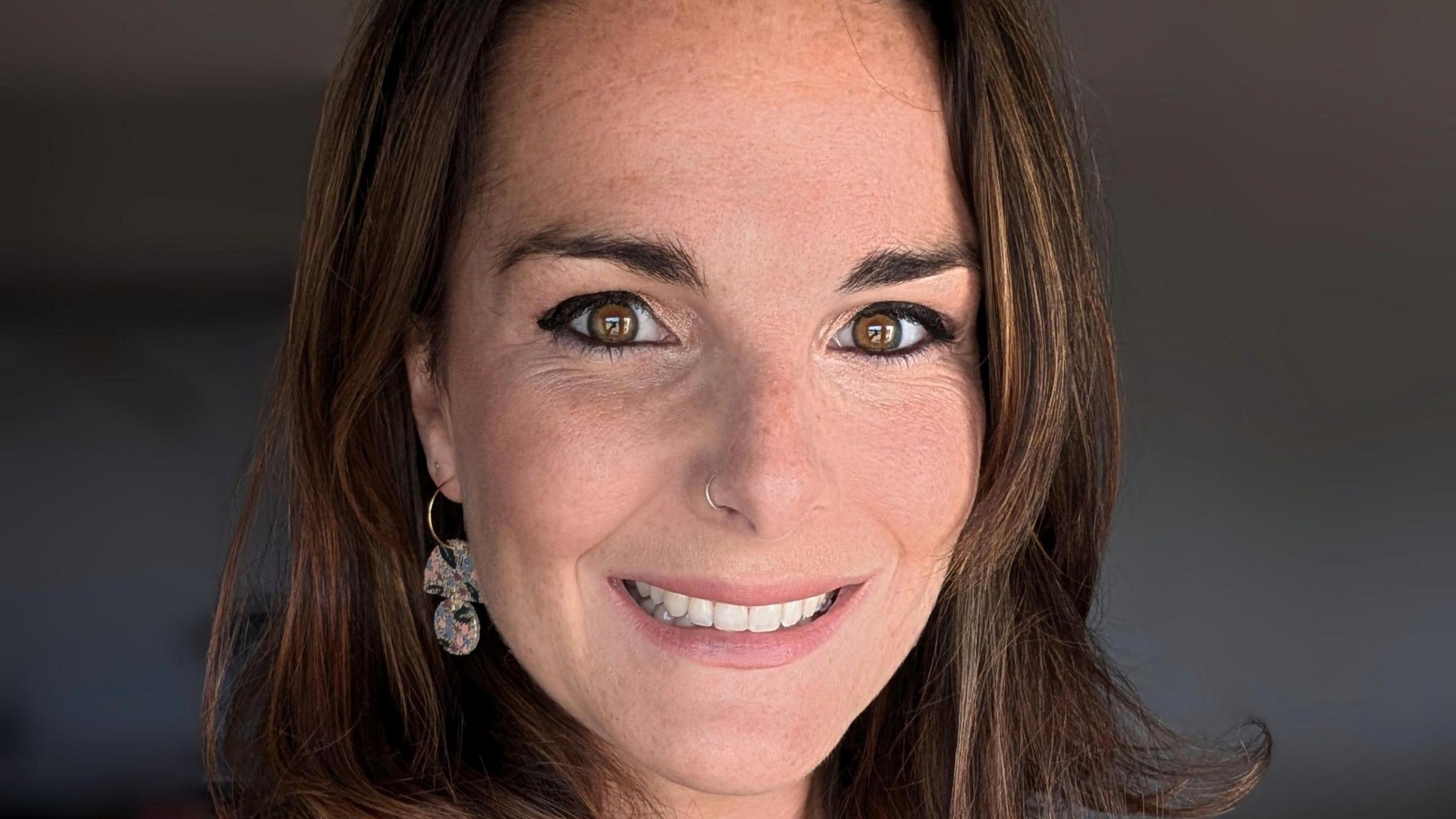 Portrait of Emma Quinn with straight brown hair, a nose ring and one dangling earring visible