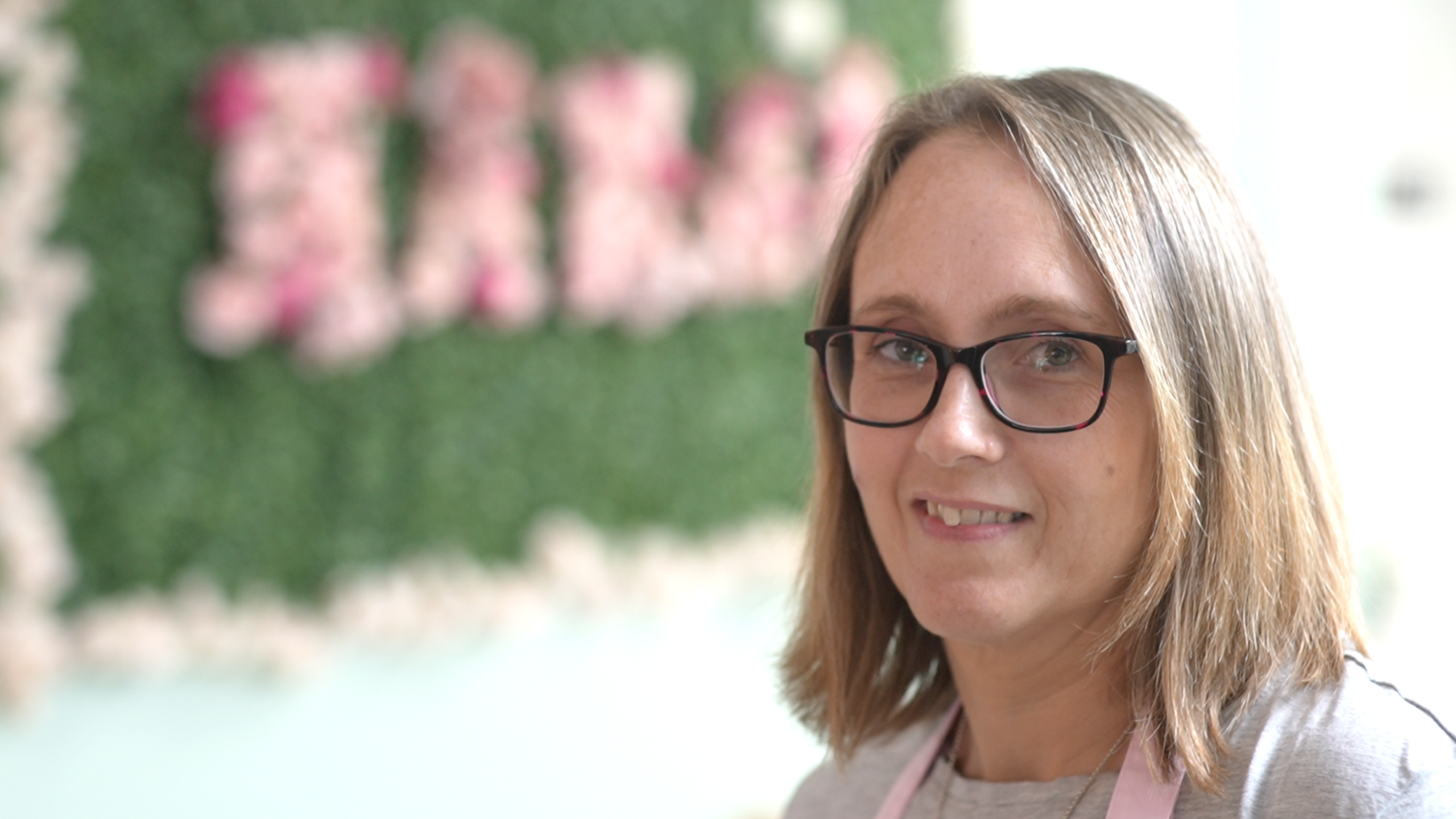 Abby Harvey, who has shoulder-length hair and is wearing glasses, looks into the camera, with a green wall behind her.