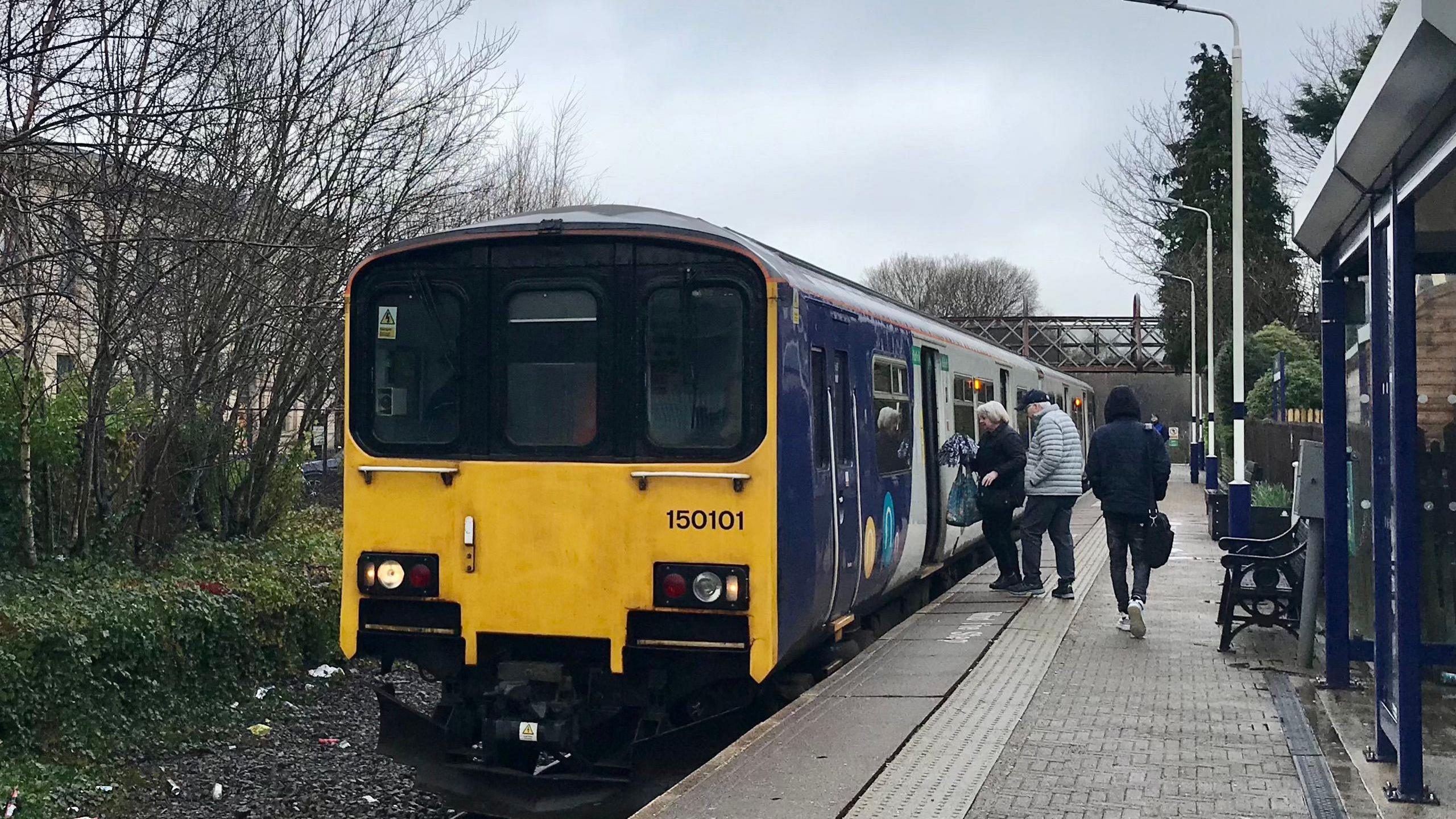 Passengers getting on a train at Brierfield railway station on single track Colne line with Northlight mill development on the left.