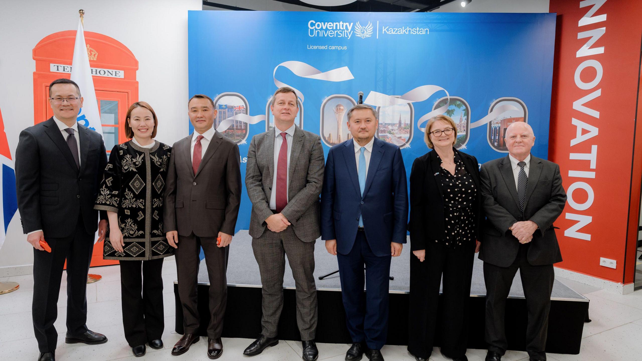 A number of men and women stand together in front of a large Coventry University and Kazakhstan board.