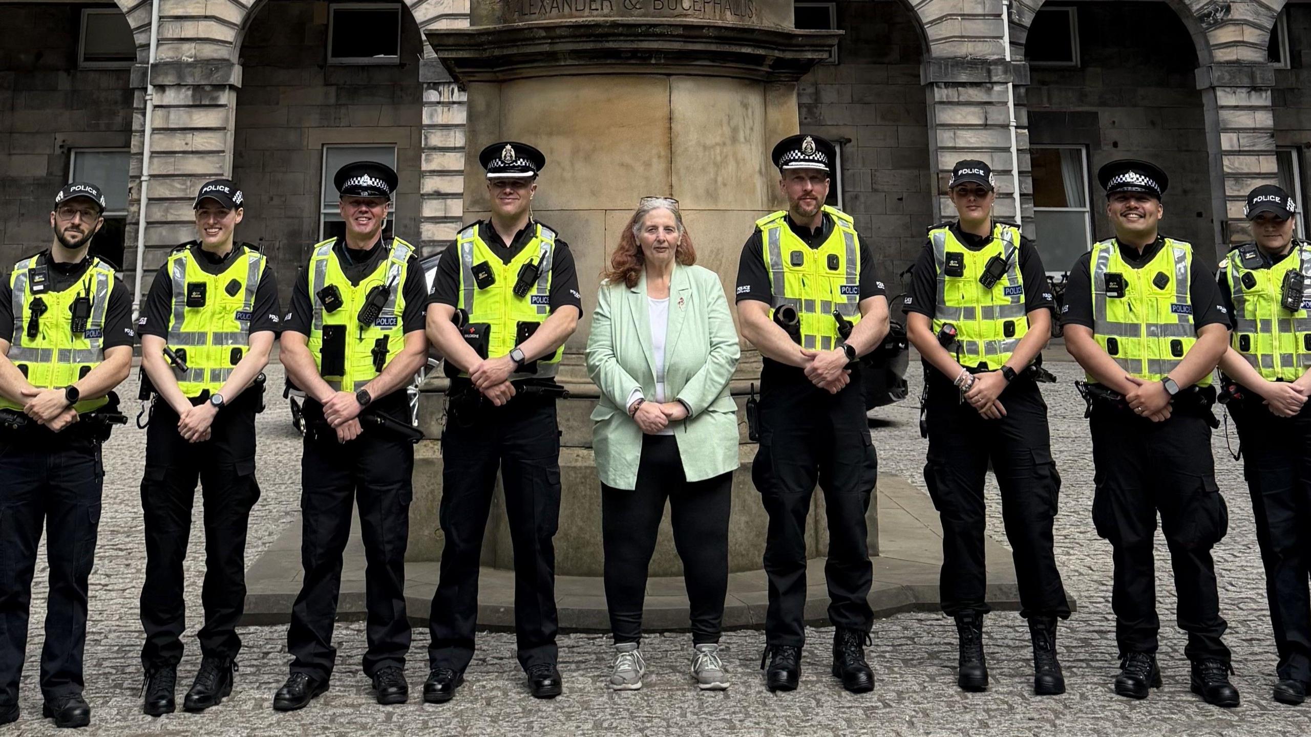 Uniformed police officers standing in a row in front of the City Chambers. Councillor Margaret Graham, who is wearing a mint green blazer and black trousers stands in the middle. 