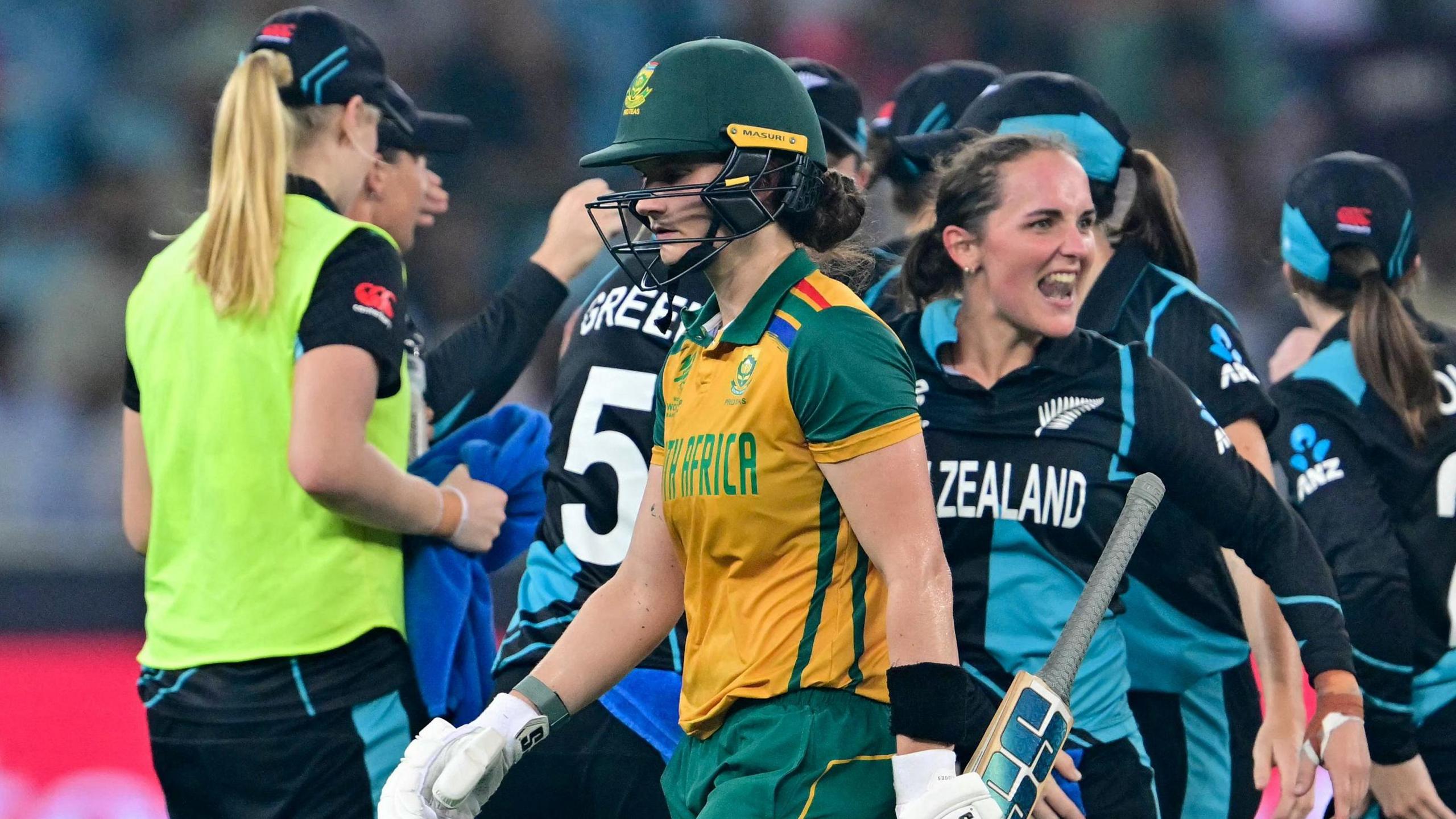 South Africa's Laura Wolvaardt holds her bat in her left hand as she trudges off the pitch as New Zealand players celebrate in the background during the T20 World Cup final