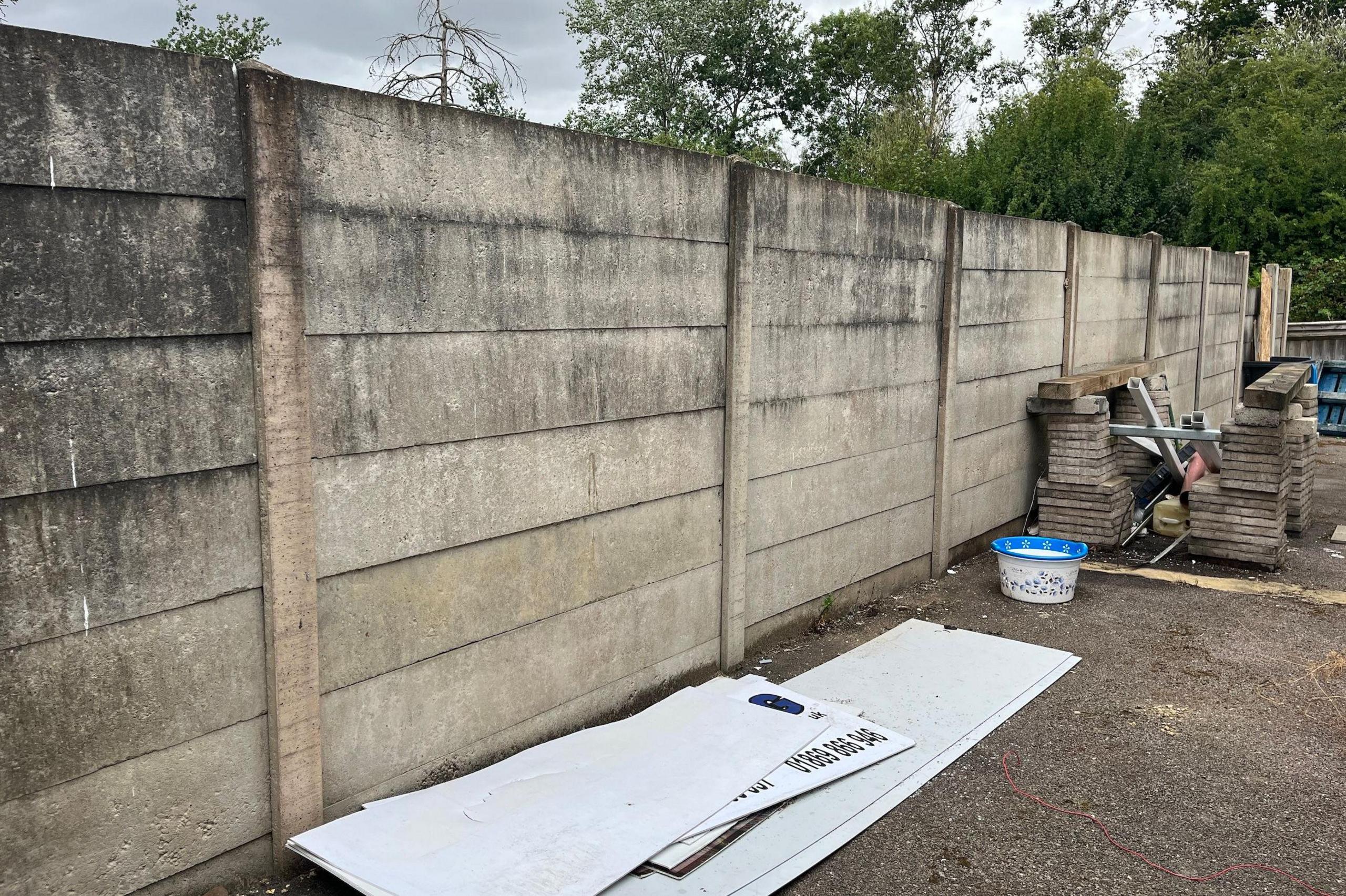 A row of concrete fence panels, with trees in the background.