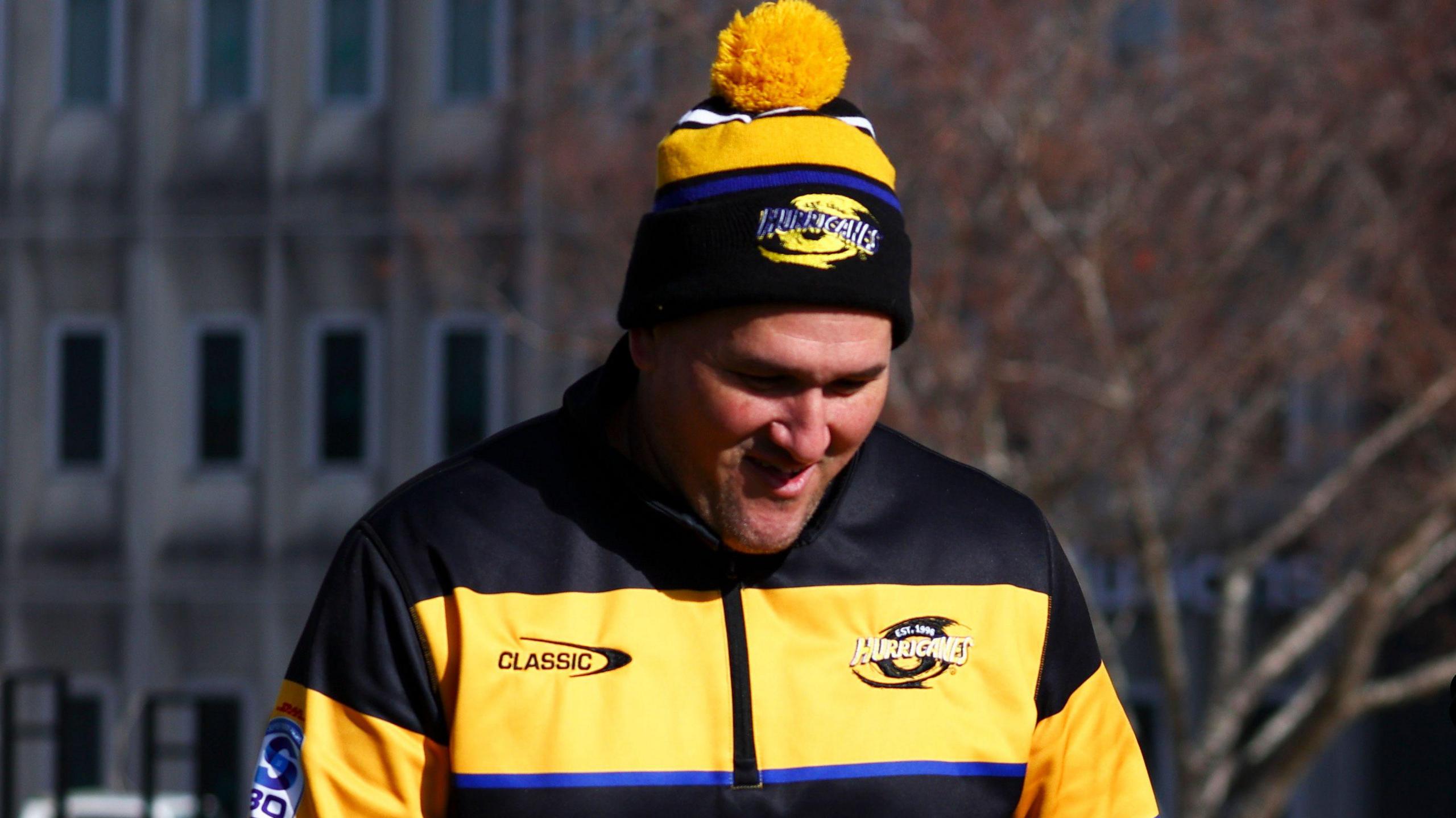 Brad Cooper in a yellow and black jacket and bobble hat, smiling with his head bowed slightly