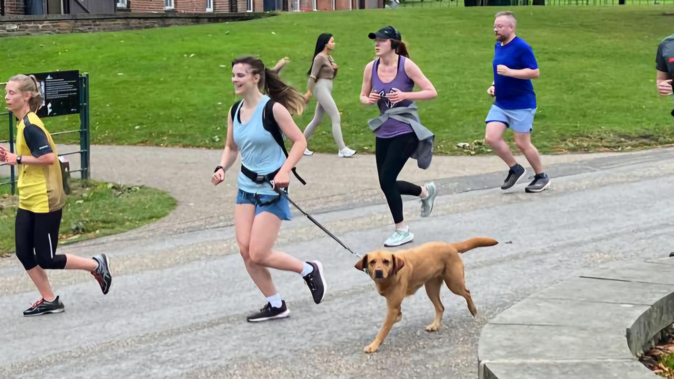 Kelsey Sheridan is running alongside her assistance dog Hamble. She is wearing a belt with a lead attached.
