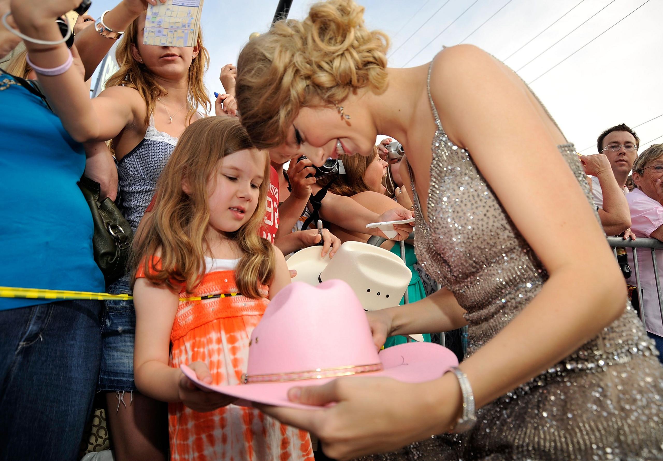 Taylor Swift signs a young fan’s cowboy hat.