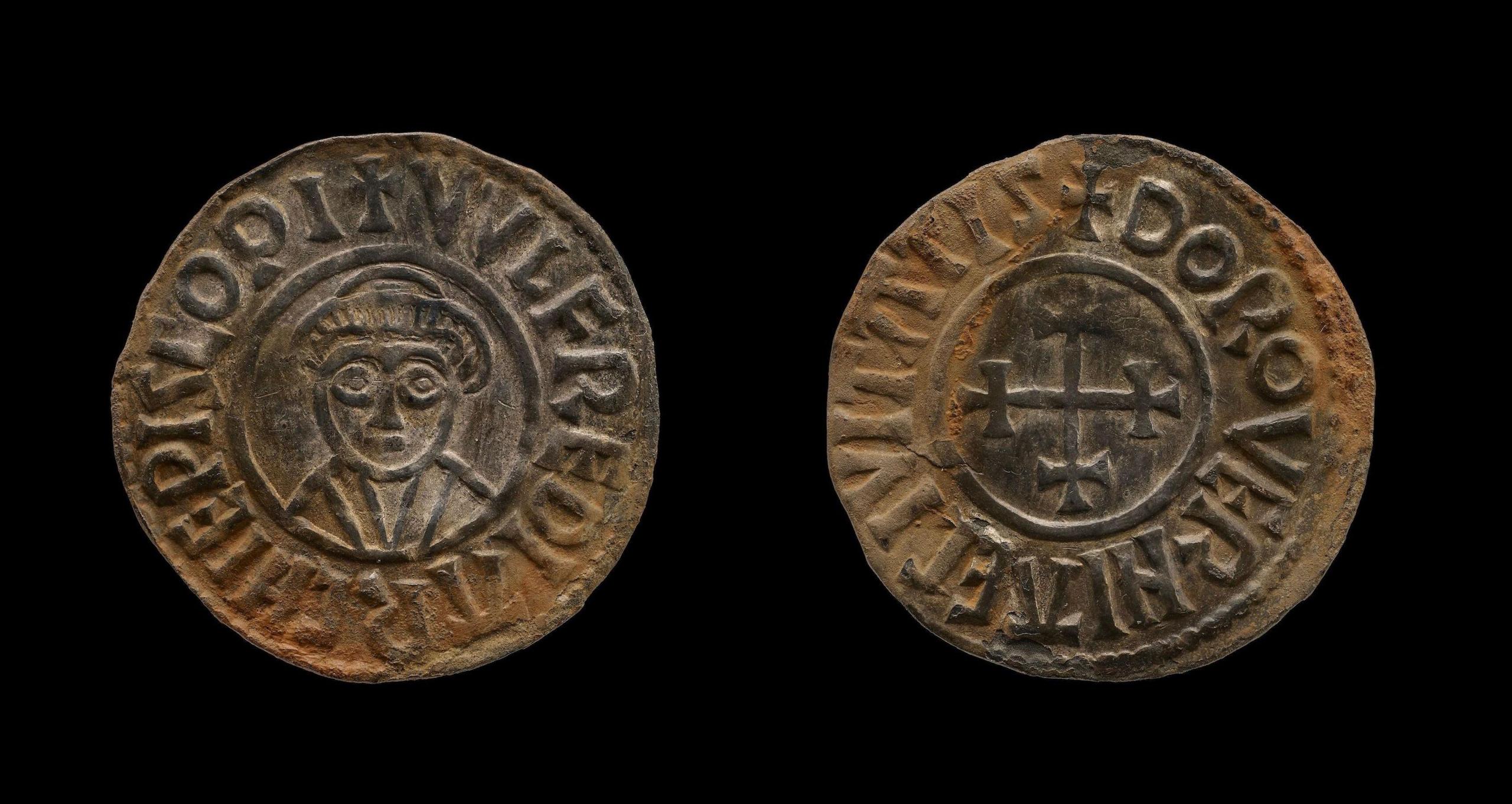 A small, silver coin, showing a bishop on one side and a cross on the other