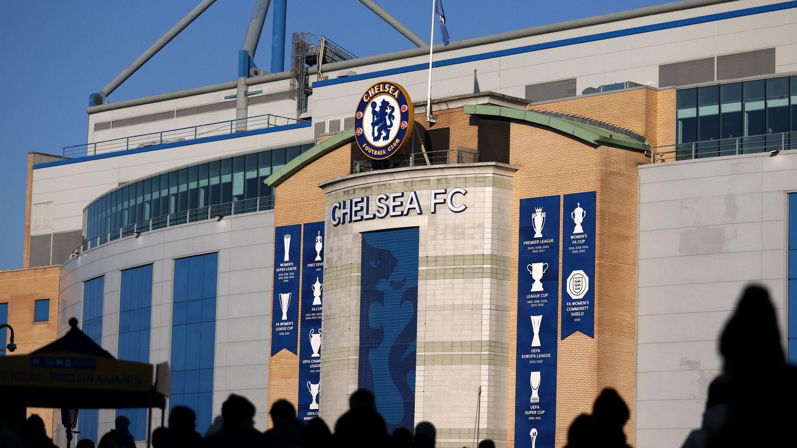 The exterior of Stamford Bridge,  Chelsea FC's stadium, with a giant version of the club's crest on display, along with banners celebrating the trophies it has won.