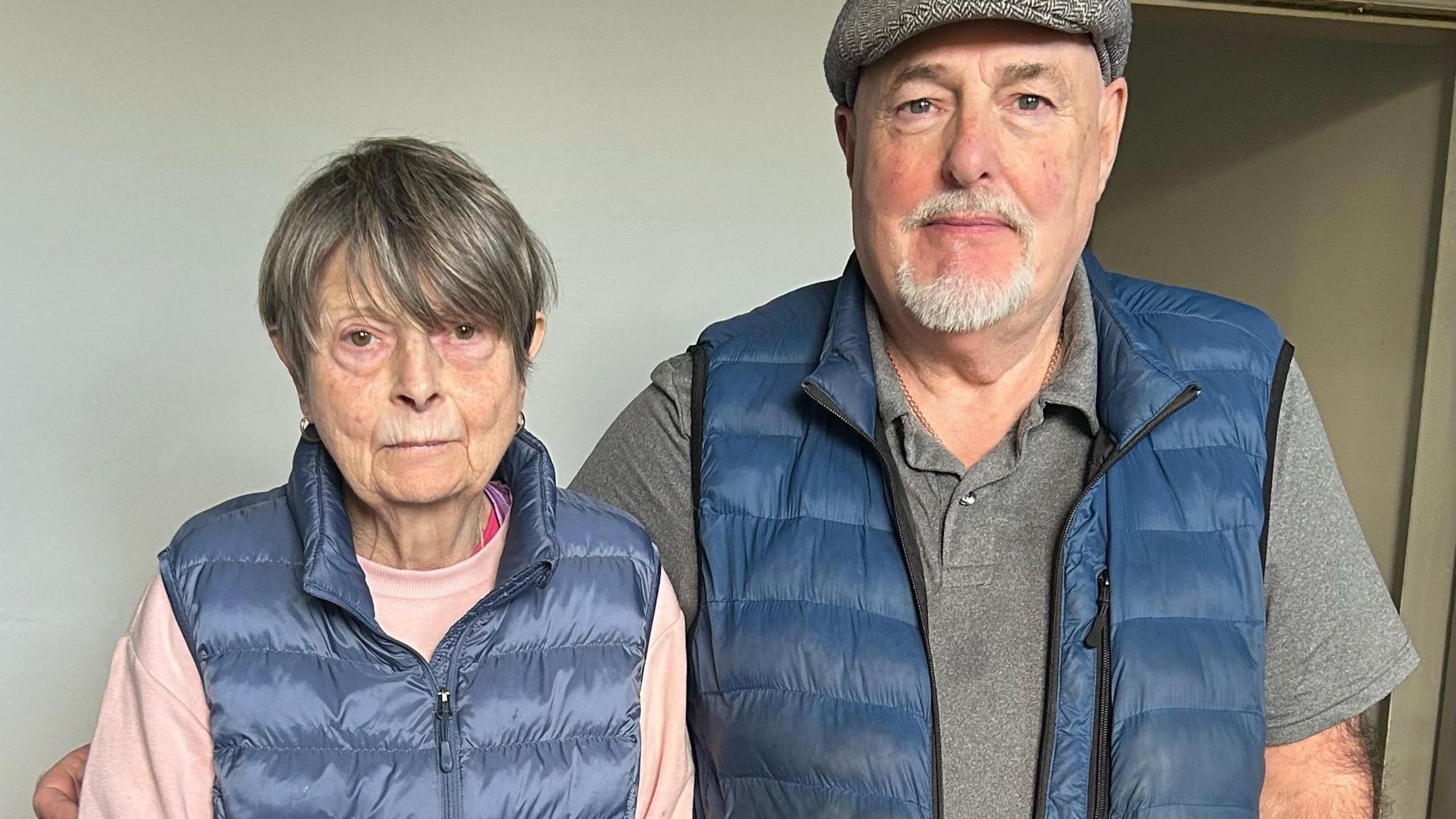 Head and shoulders shot of Pat Bailey on the right and her husband David Bailey. They are both wearing blue gilets and David has a flat cap on.