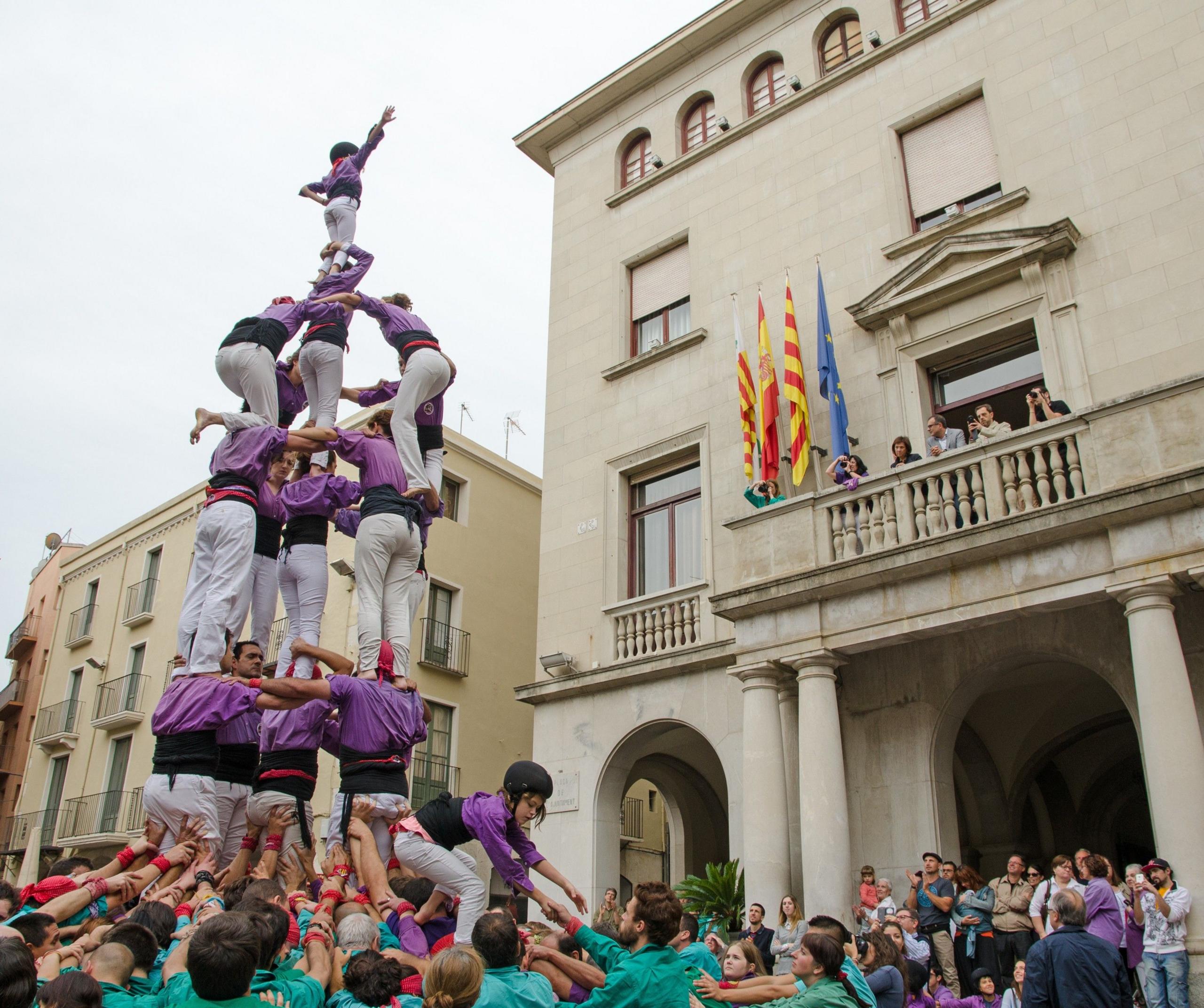 People dressed in purple and white are boosted on top of each other to form a tower 