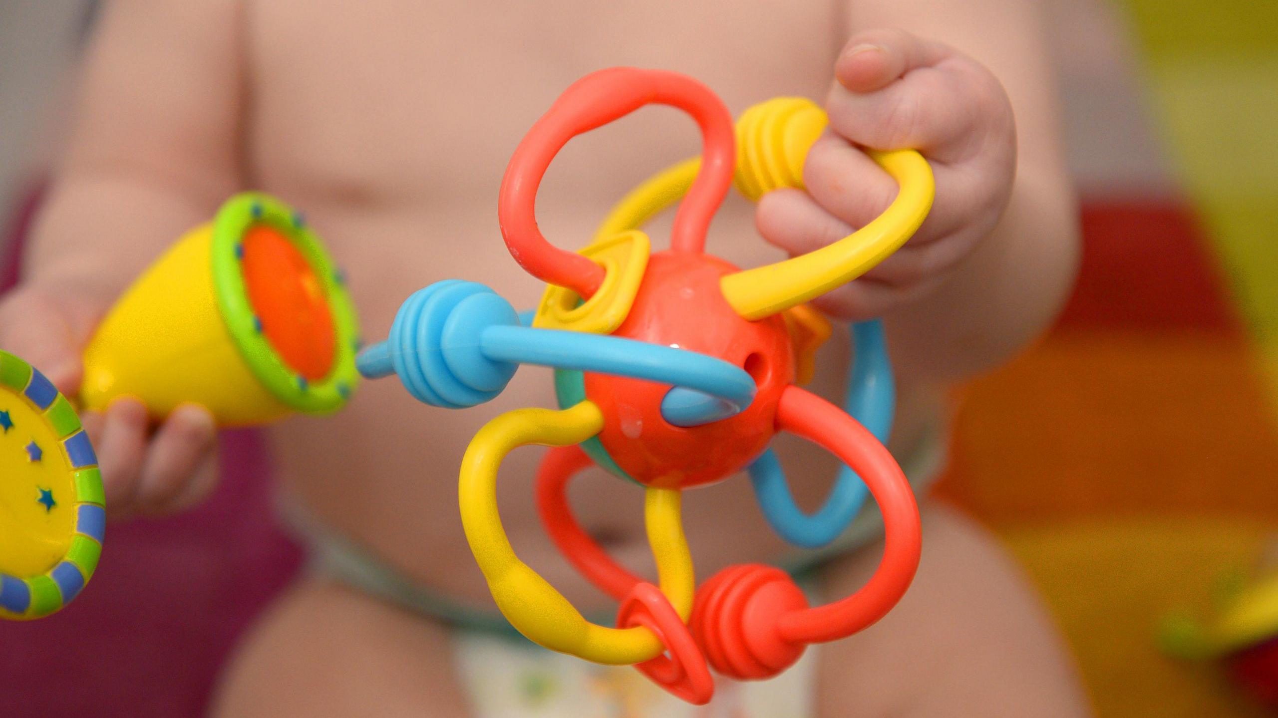 An image of an unidentifiable baby playing with a brightly coloured toy.