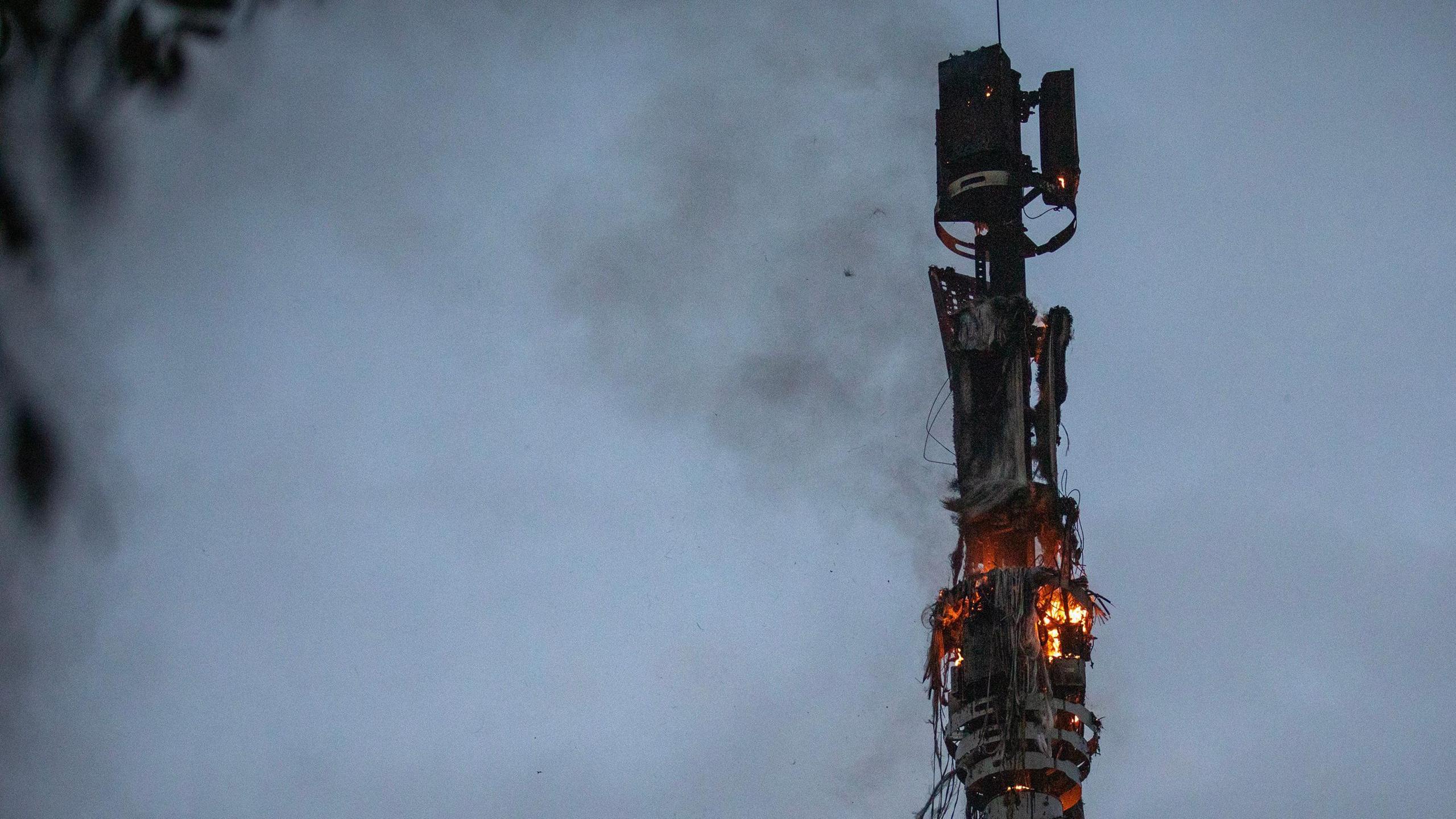 A 5G mast on fire in west Belfast - the fire has been mostly put out and the charred remains are what is left, but there are still some flames on it.