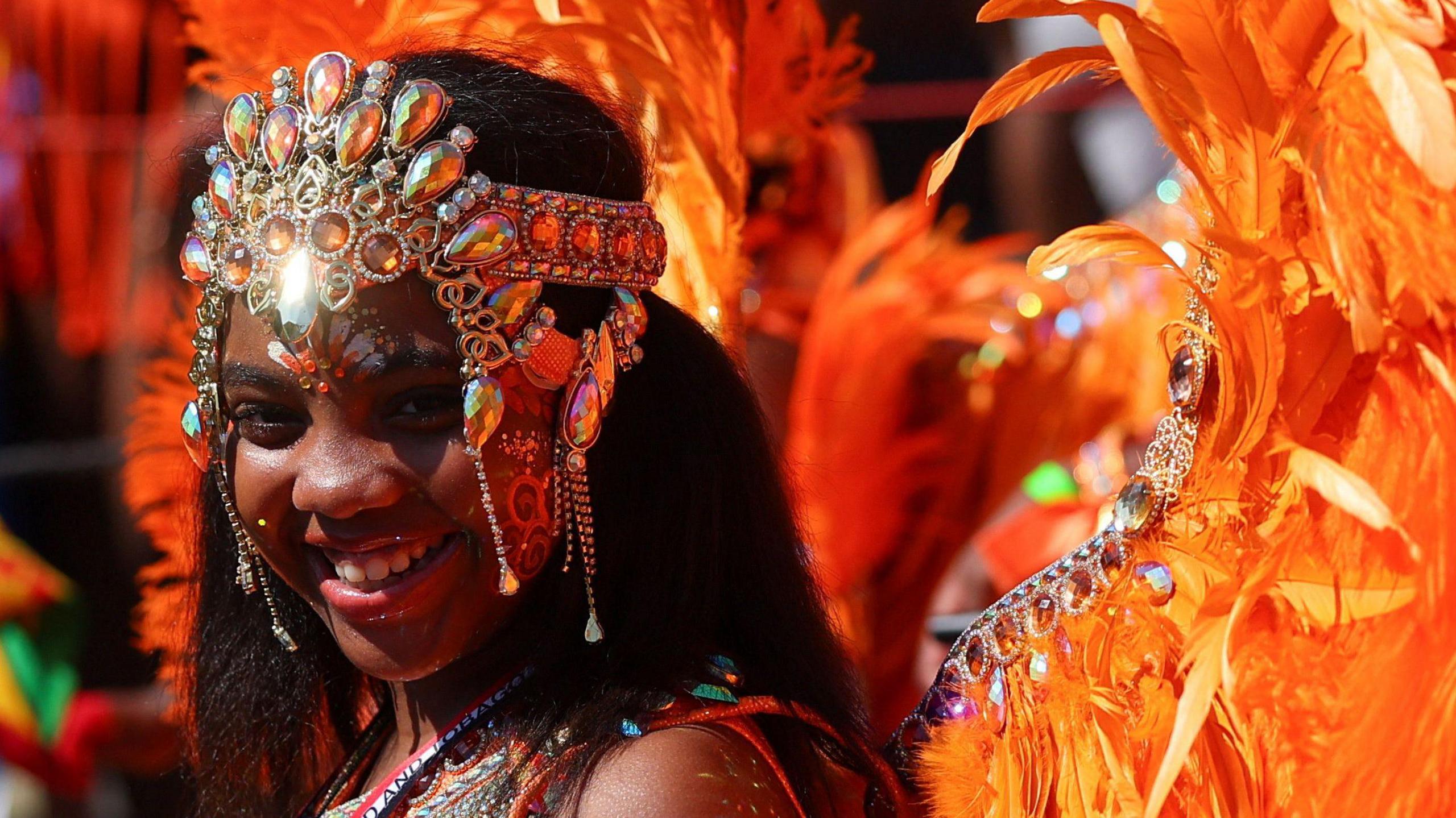 A child in an orange feathered outfit smiles during the Children's Day Parade.