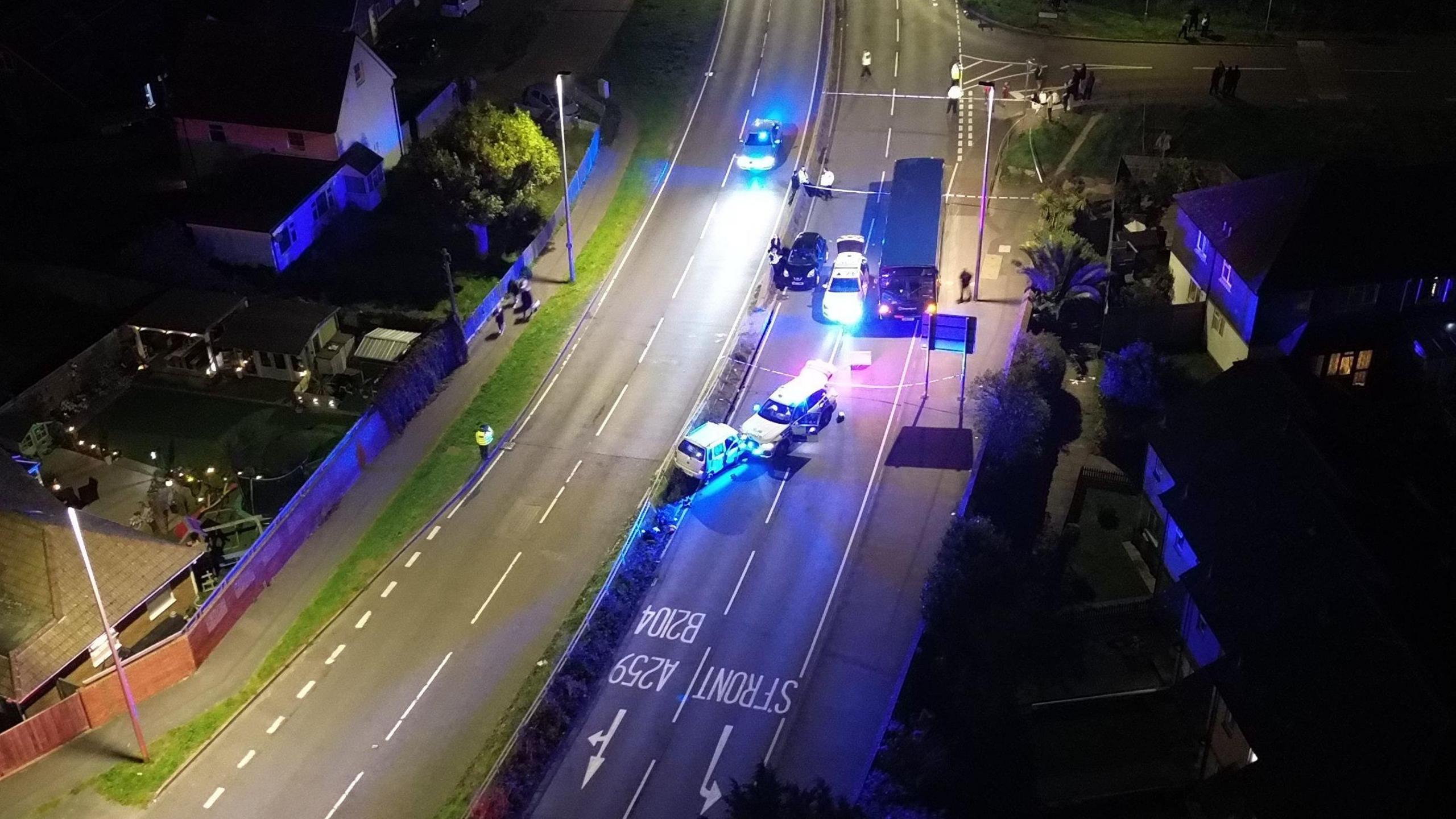 An aerial view of a crash involving a marked police car and a grey vehicle. There are emergency services attending the incident.