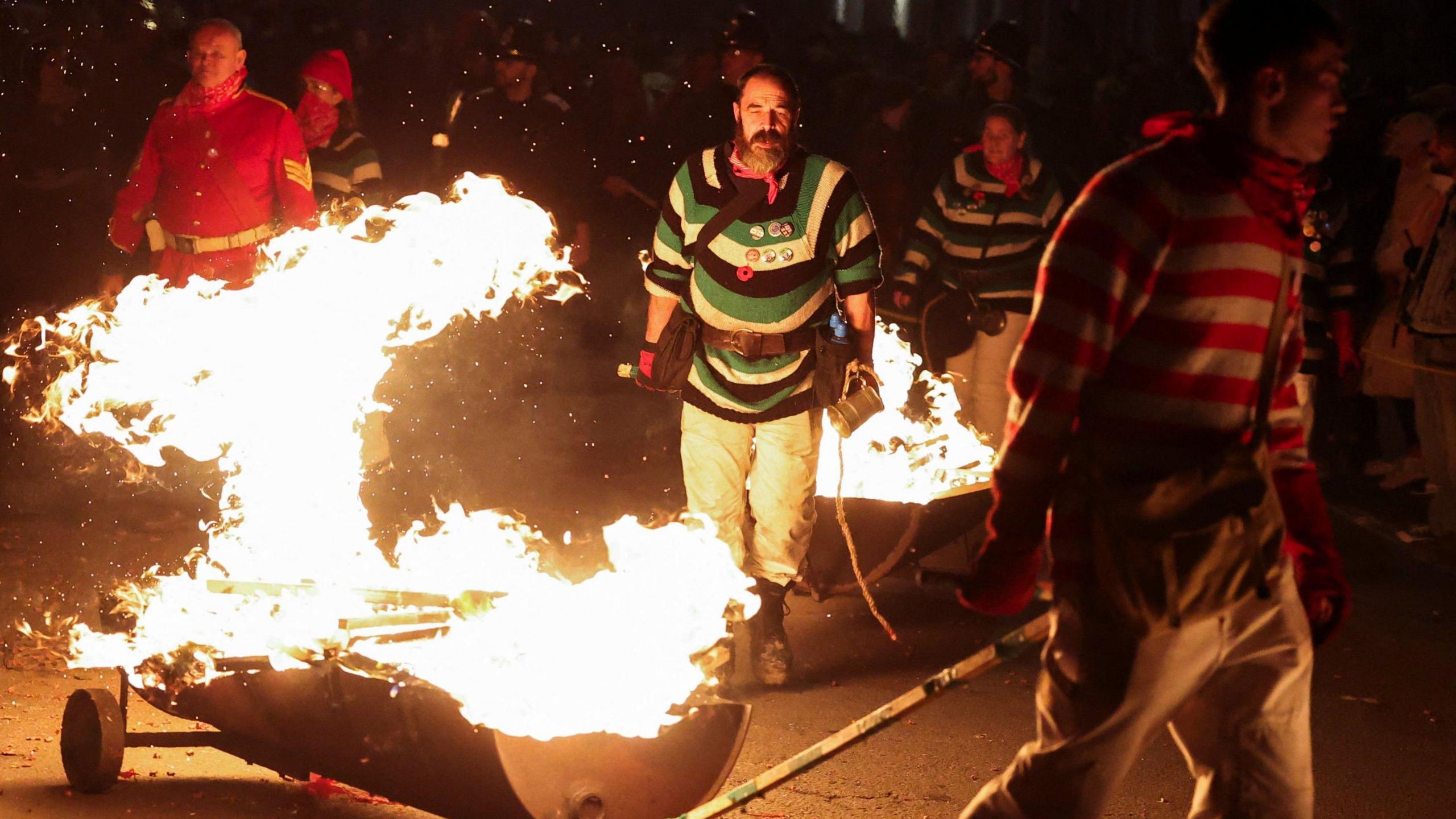Members of a bonfire society drag half-oil drums alight with small bonfires through the streets of Lewes.