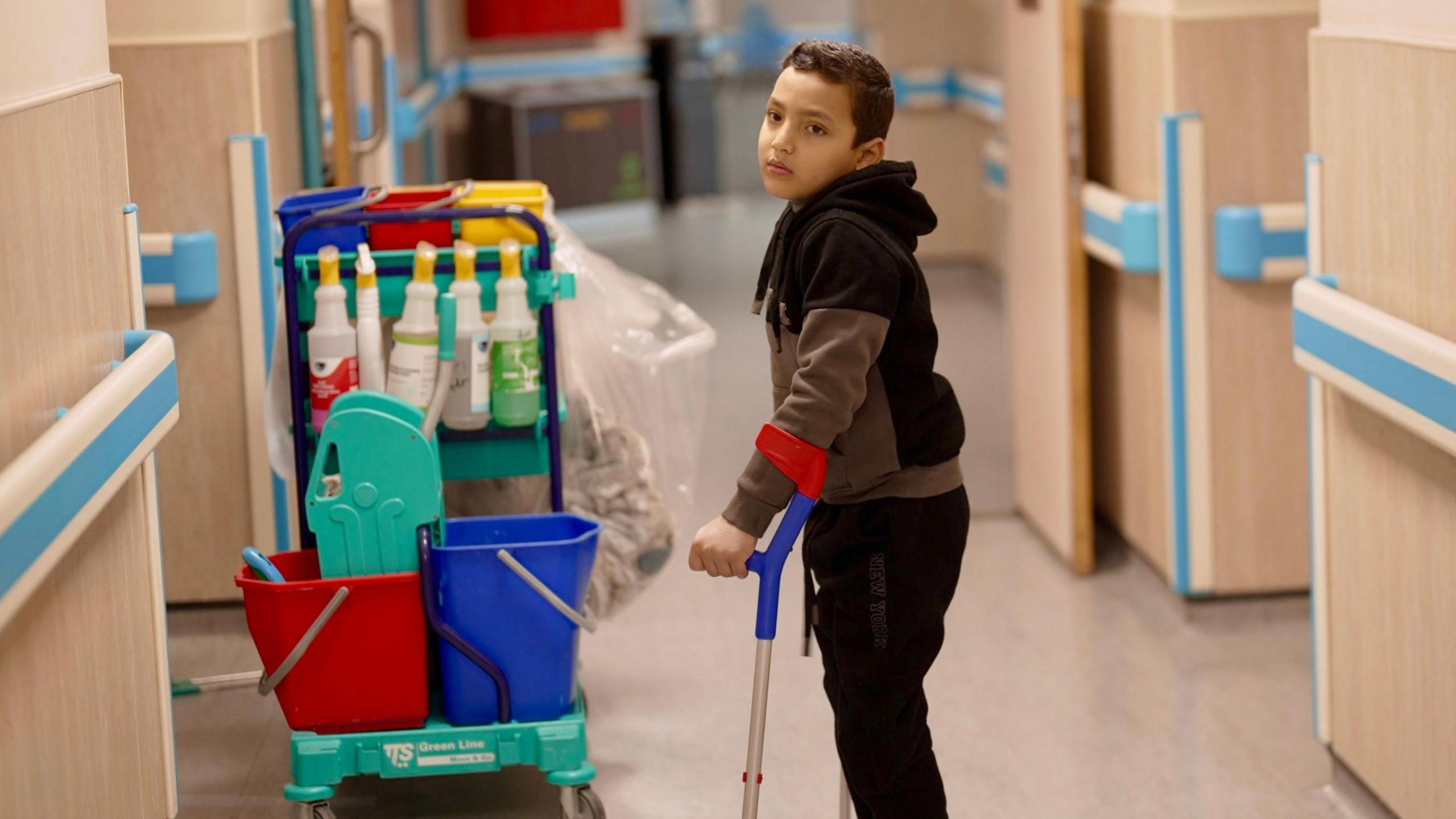 A boy using crutches is seen in a hospital corridor