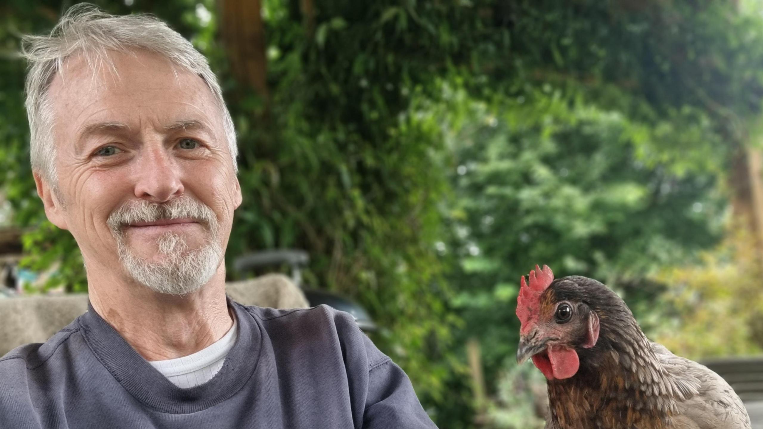 Huw Irranca-Davies on a chair in a garden with a rooster