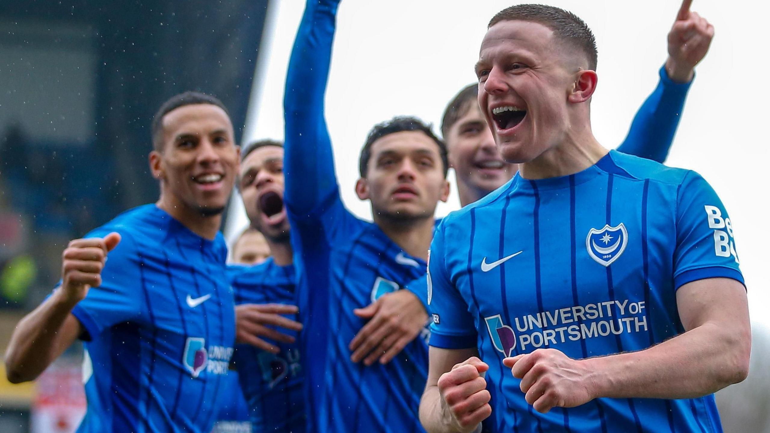 Colby Bishop celebrates Portsmouth going ahead at Oxford United's Kassam Stadium while goalscorer Andre Dozzell is congratulated in the background.