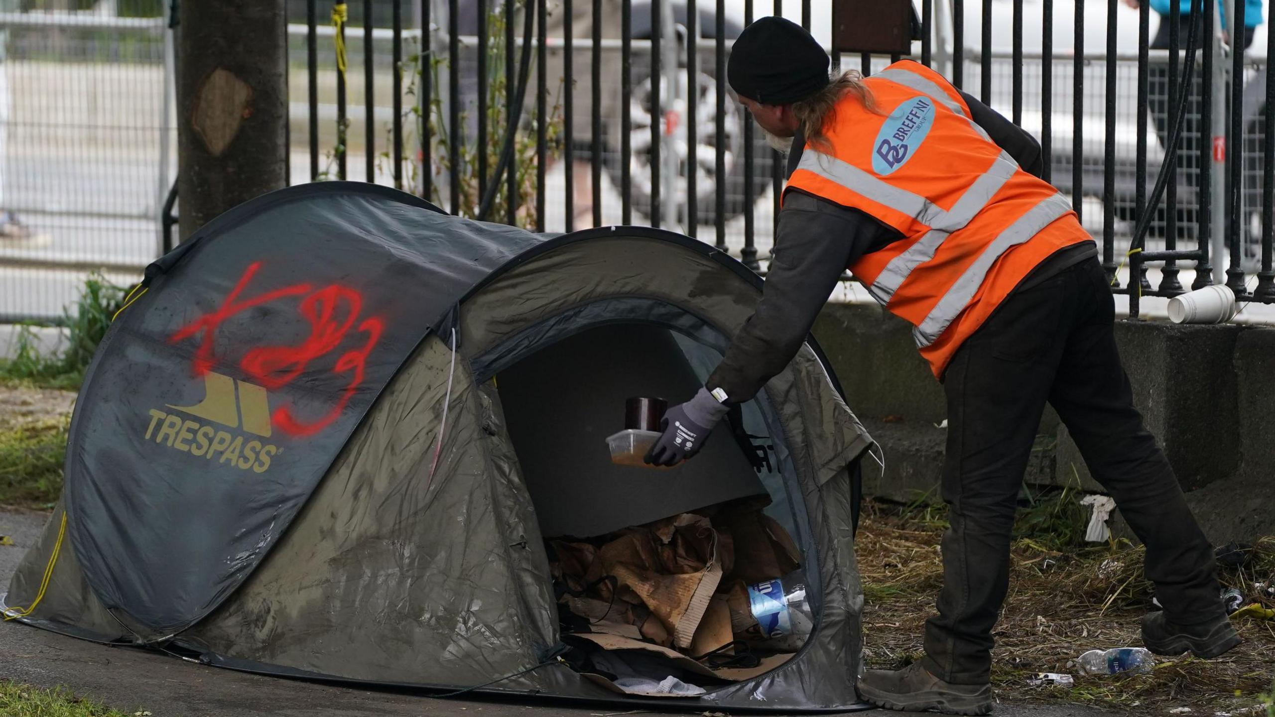 A worker in a high viz orange vest clearing rubbing from a green tent in Dublin