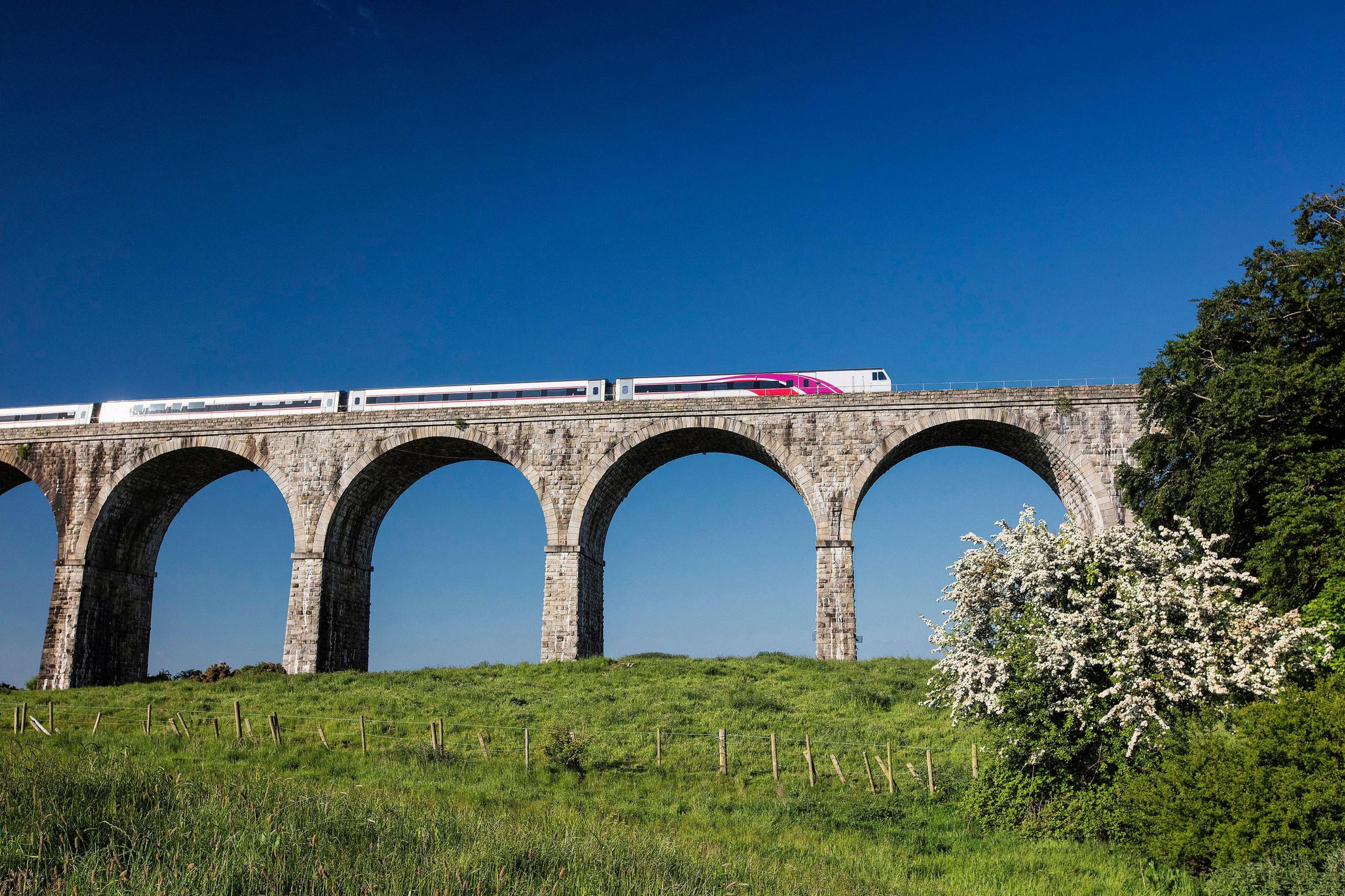 Dublin to Belfast train travelling on raised railway bridge with arched columns with green fields underneath