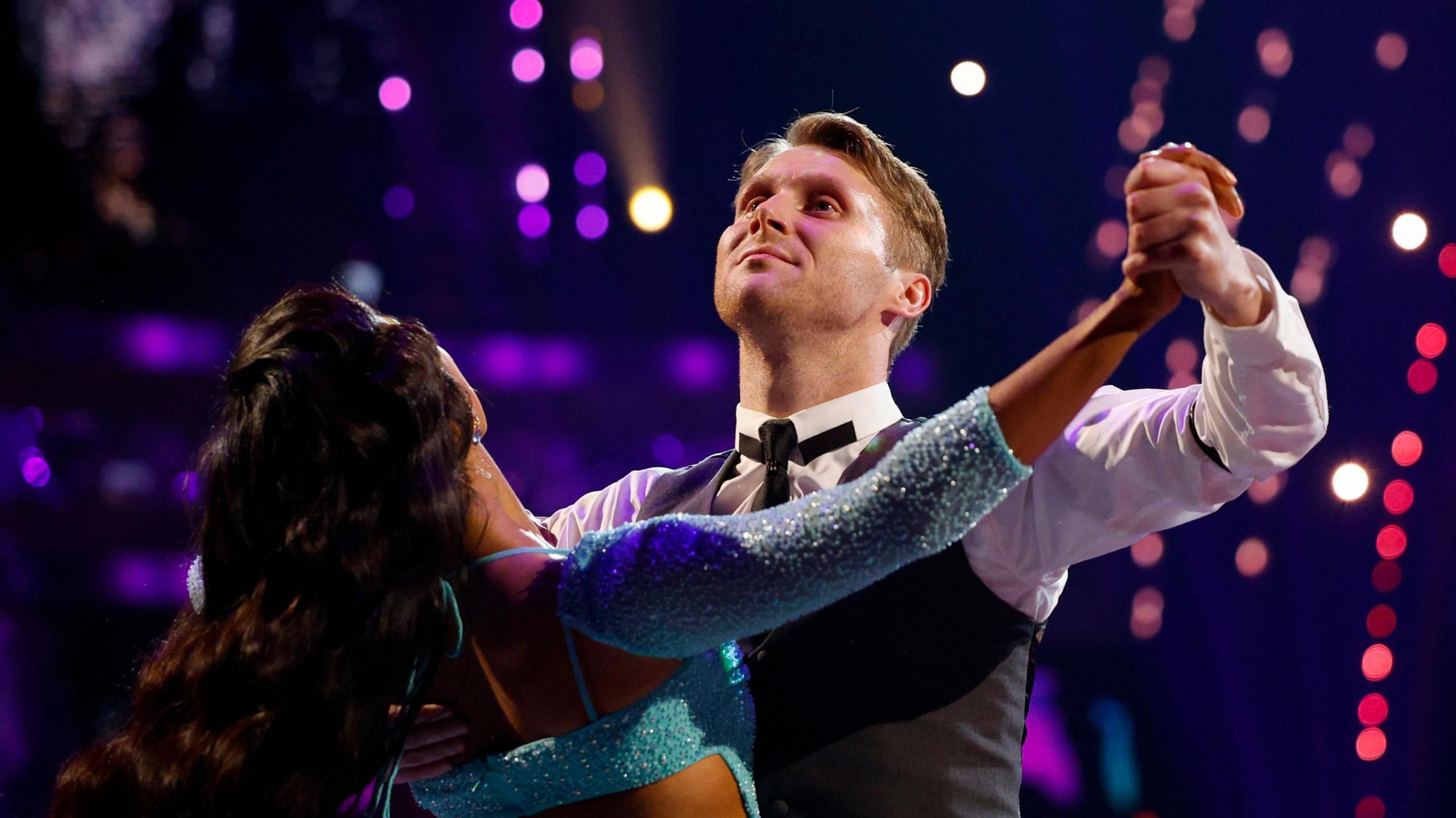 A man in a tuxedo spins his partner around on the dancefloor