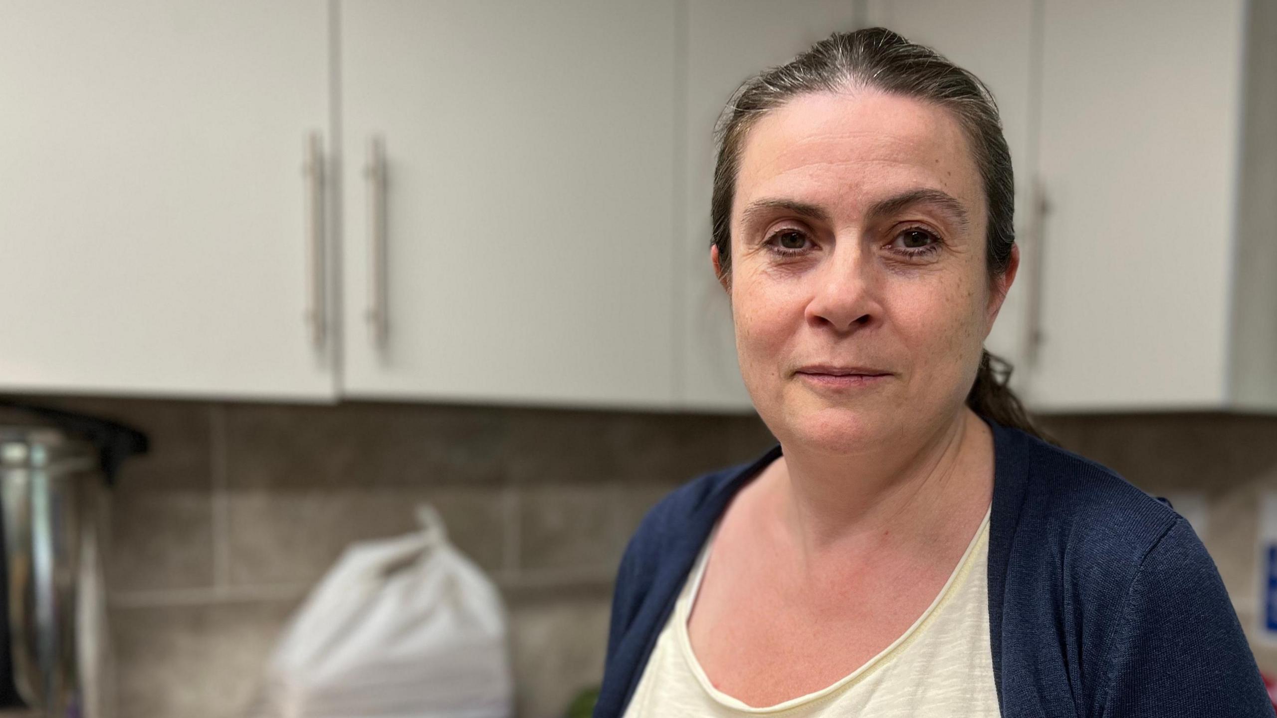 Image shows Family Voice Peterborough CEO Louise Ravenscroft standing in a kitchen. In the background there are groceries in clear packaging. 